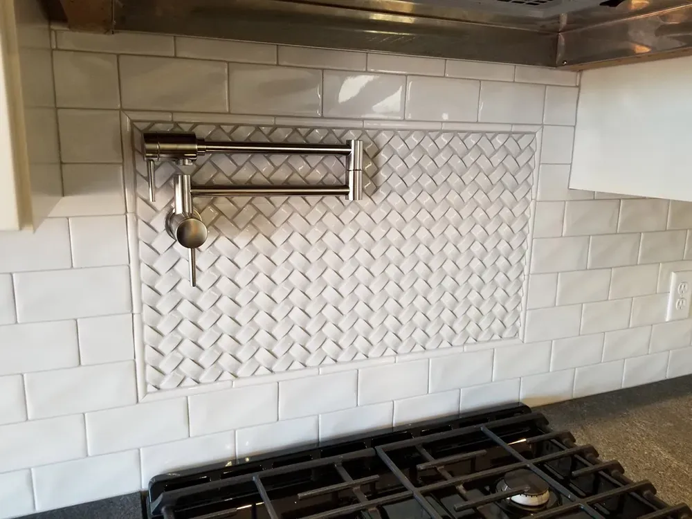 A kitchen backsplash featuring a white subway tile wall with a central, rectangular inset of woven white marble tiles.