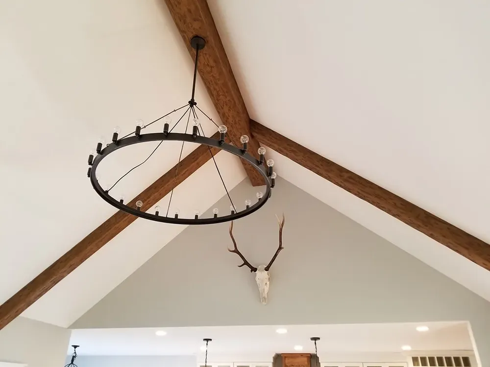 A vaulted ceiling features dark wood beams and a large, black circular chandelier hanging above a deer skull wall mount.