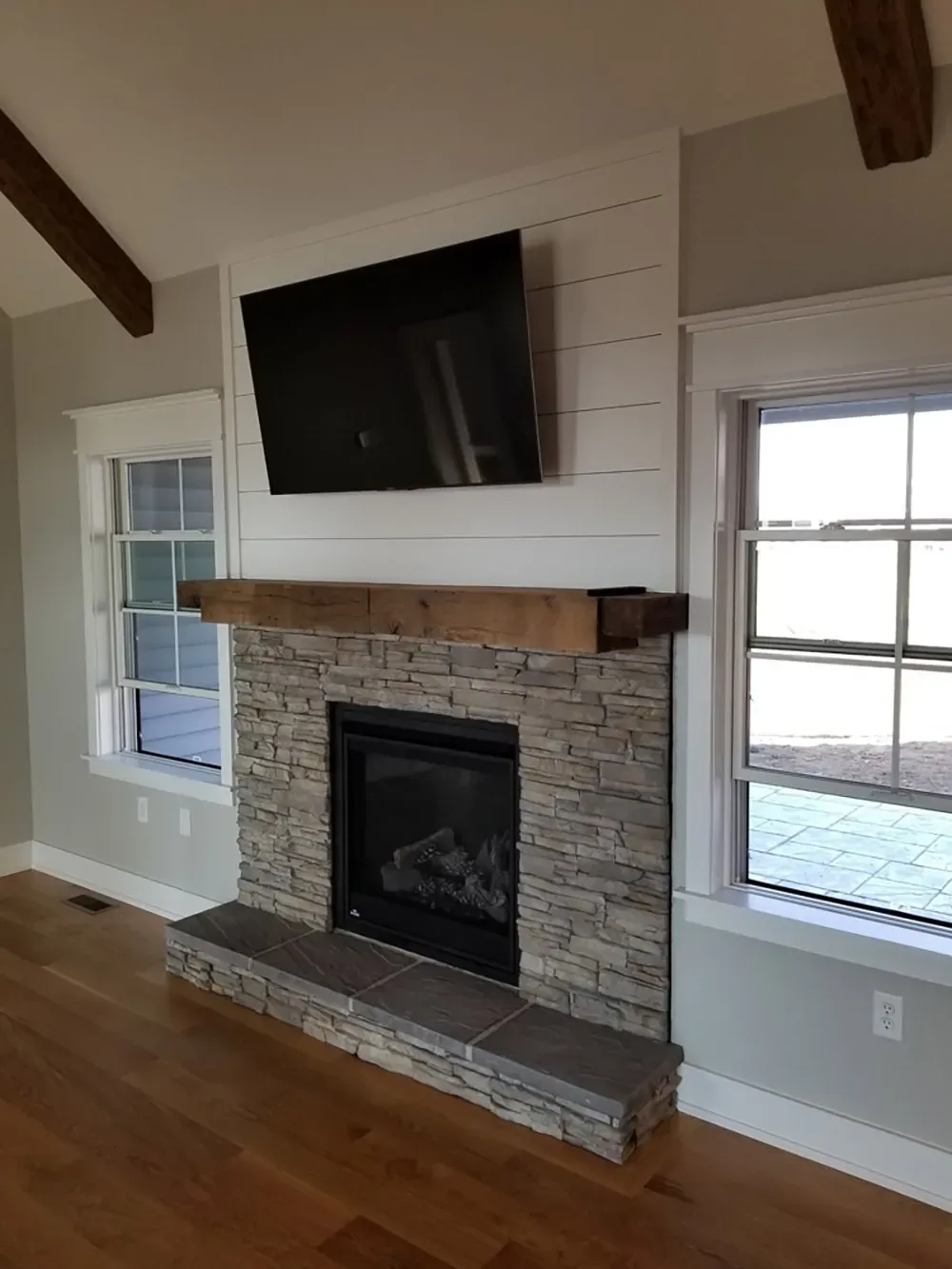 A fireplace with a stone hearth and surround, a wooden mantel, and a wall-mounted TV on a white shiplap accent wall.