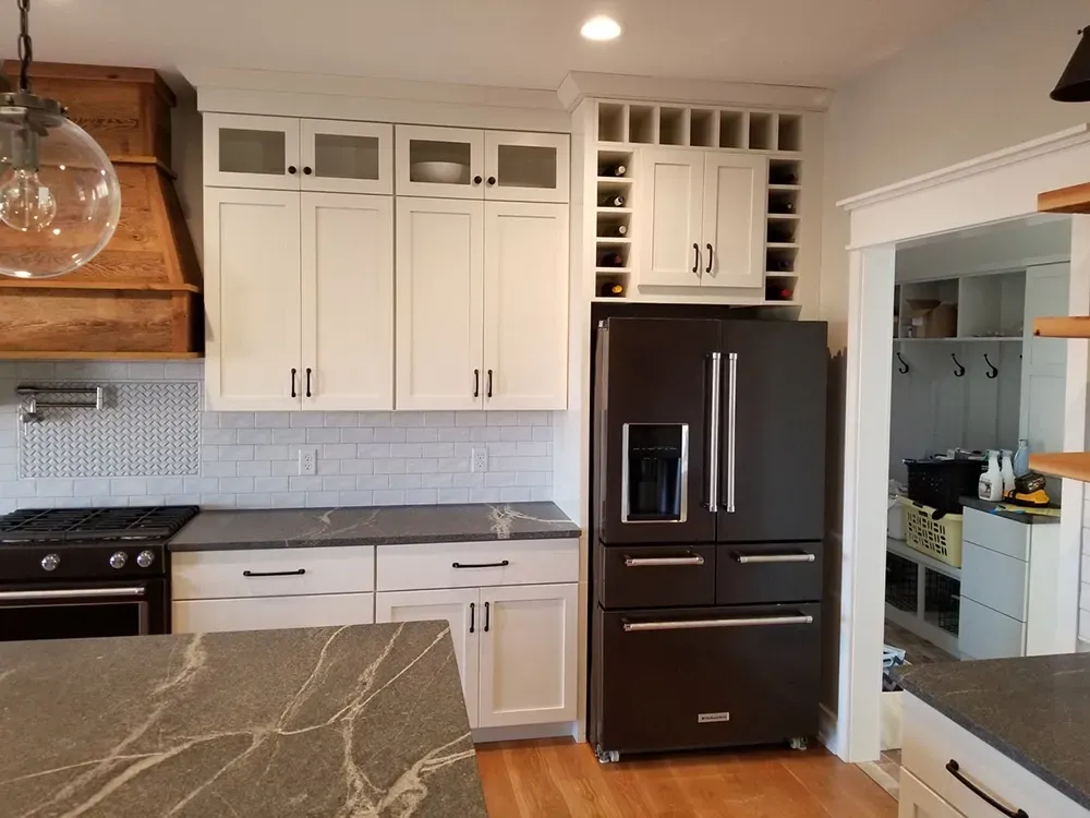 A kitchen featuring white cabinets, a black refrigerator, dark stone countertops, and a wood vent hood above a stove.