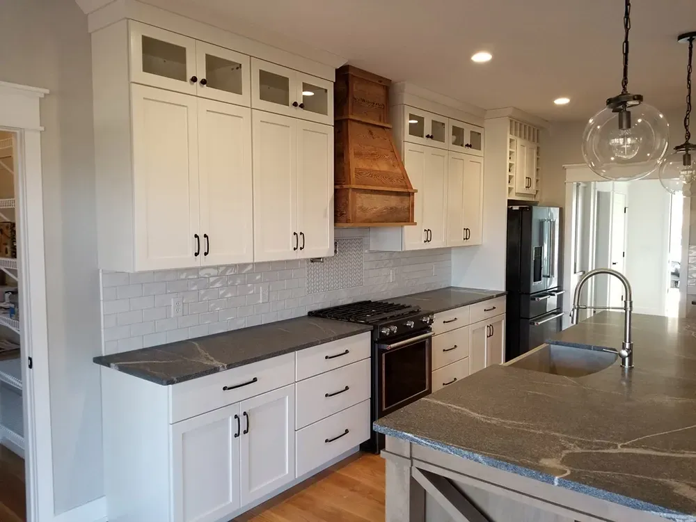 Modern kitchen with white shaker cabinets, dark stone countertops, a wooden range hood, and a central island.