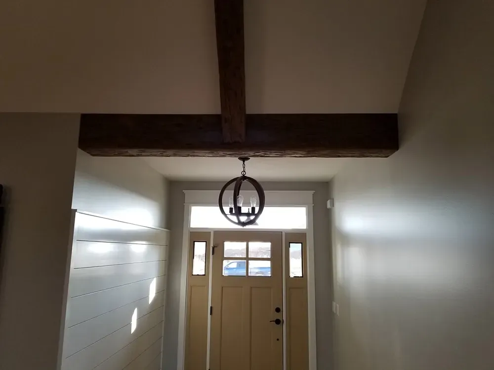 An entryway with a wooden ceiling beam, a hanging orb pendant light, a light-colored front door, and white shiplap walls.