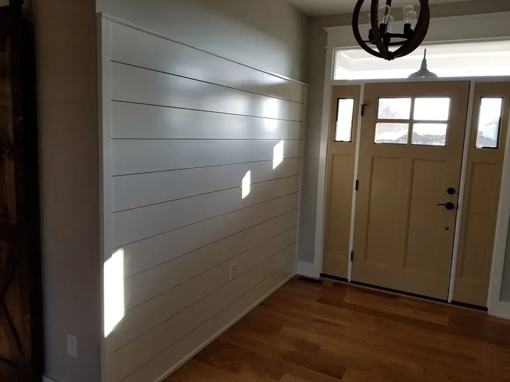 A bright foyer features a shiplap accent wall next to a wooden front door with glass panels and hardwood floors.