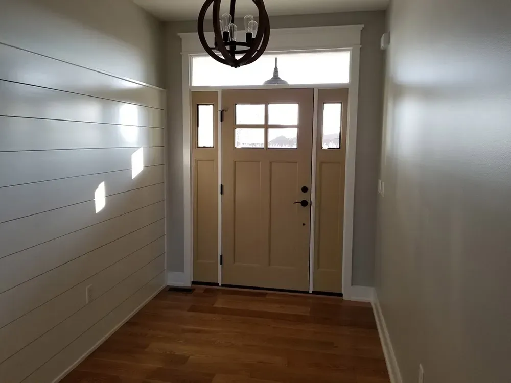 Entryway featuring a light tan front door with a transom window, hardwood floors, and a white shiplap accent wall.