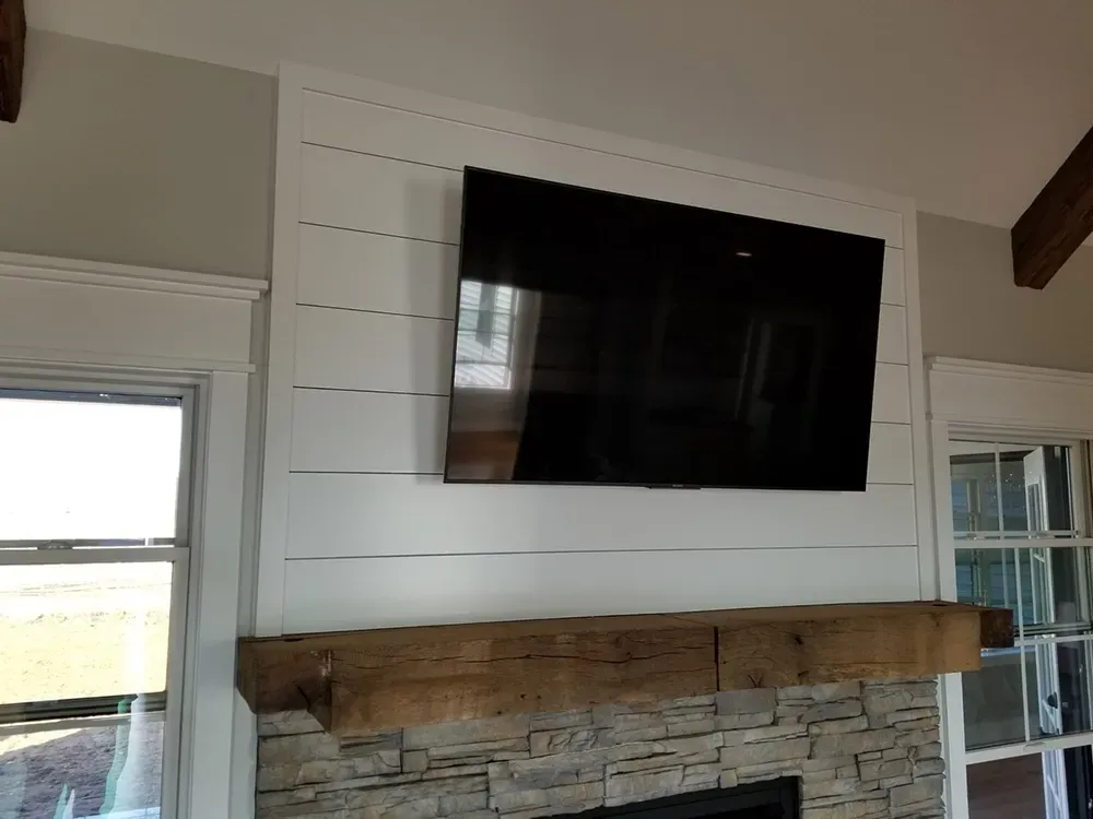 A large flat-screen TV mounted on a white shiplap accent wall above a stone fireplace with a rustic wood mantel.