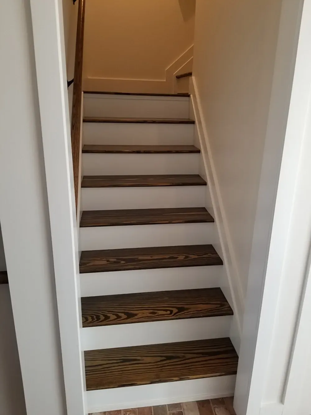 A staircase with dark wood treads and white risers viewed from the bottom looking up toward a landing.