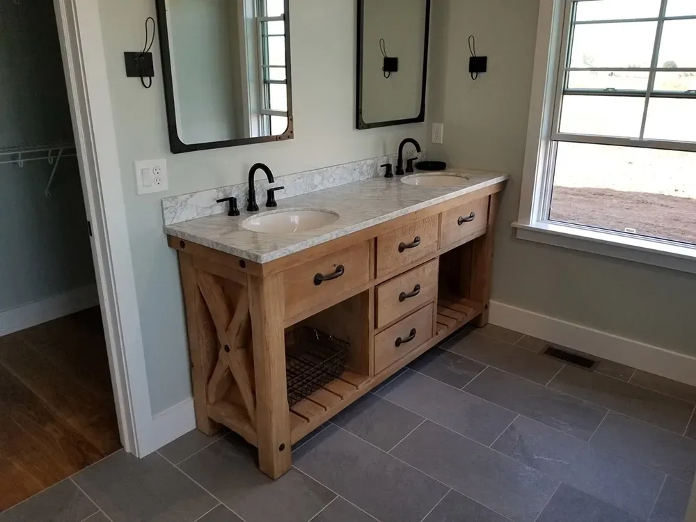 A double vanity with a marble countertop, wood base, and open shelving in a modern bathroom with grey tile floors.