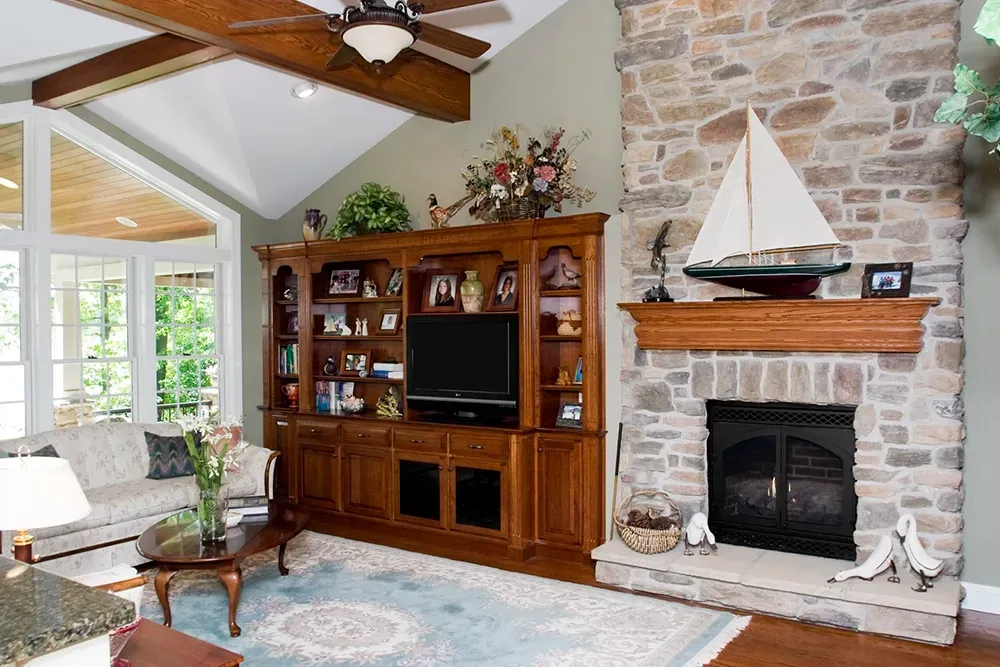 A living room with a stone fireplace, a wooden entertainment unit, a sofa, and a sailboat model on the mantel.