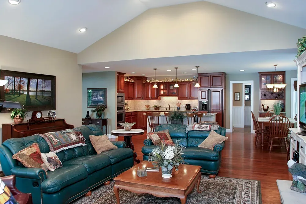 A spacious open-concept living area with a teal leather sofa, coffee table, and an adjacent kitchen with wooden cabinets.