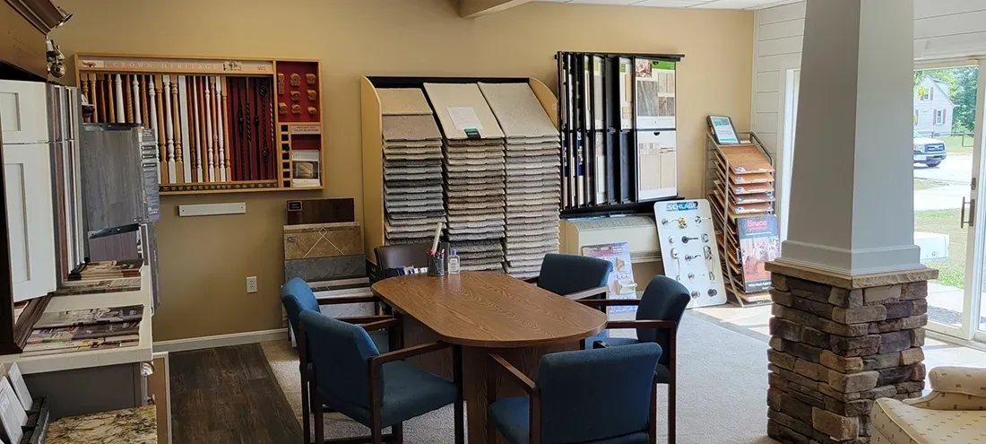 A design center office featuring a wooden meeting table surrounded by blue chairs, with walls lined by material samples.