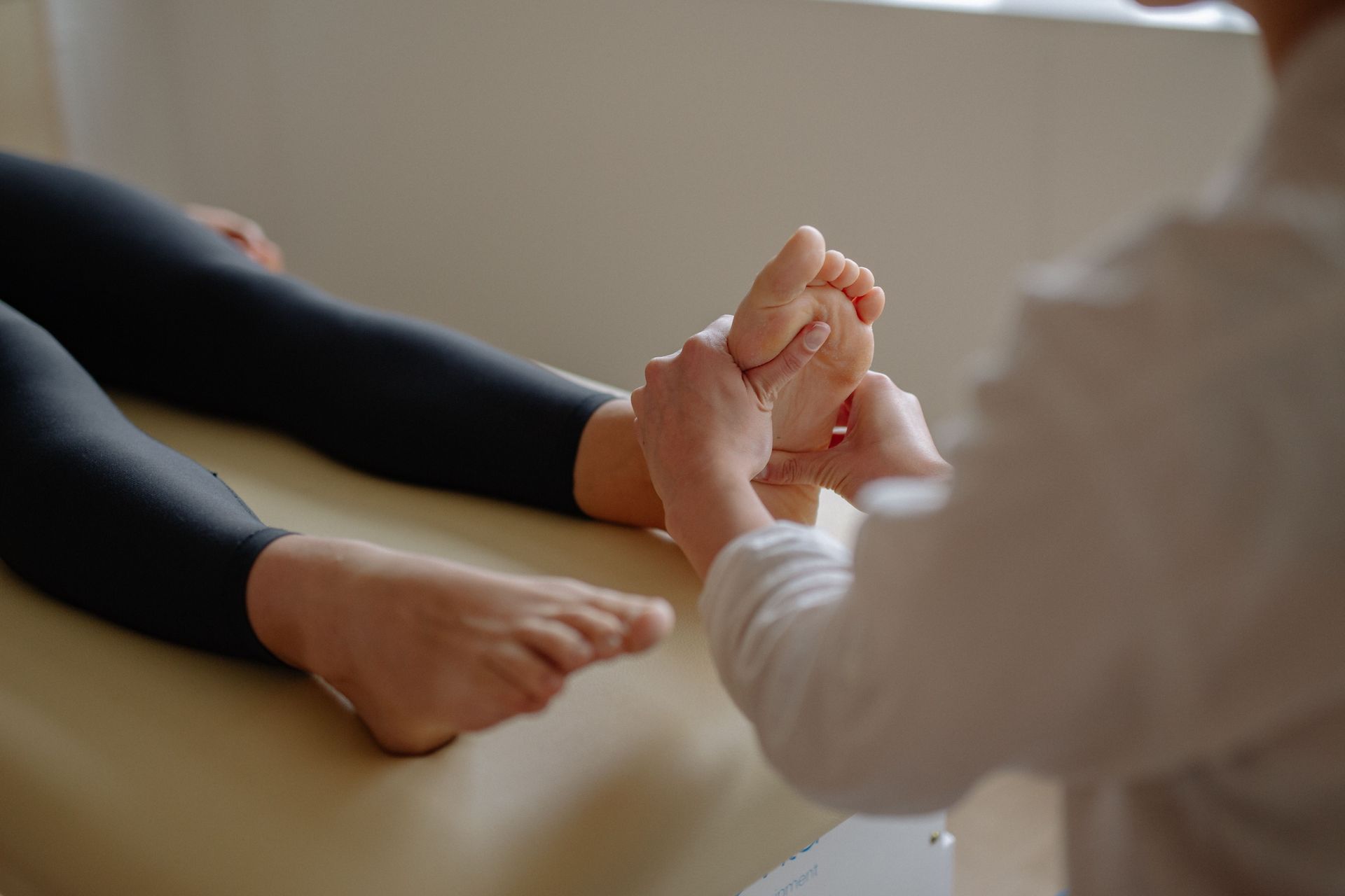 Hands clasped in a comforting gesture beside a person’s bare feet on a sofa.