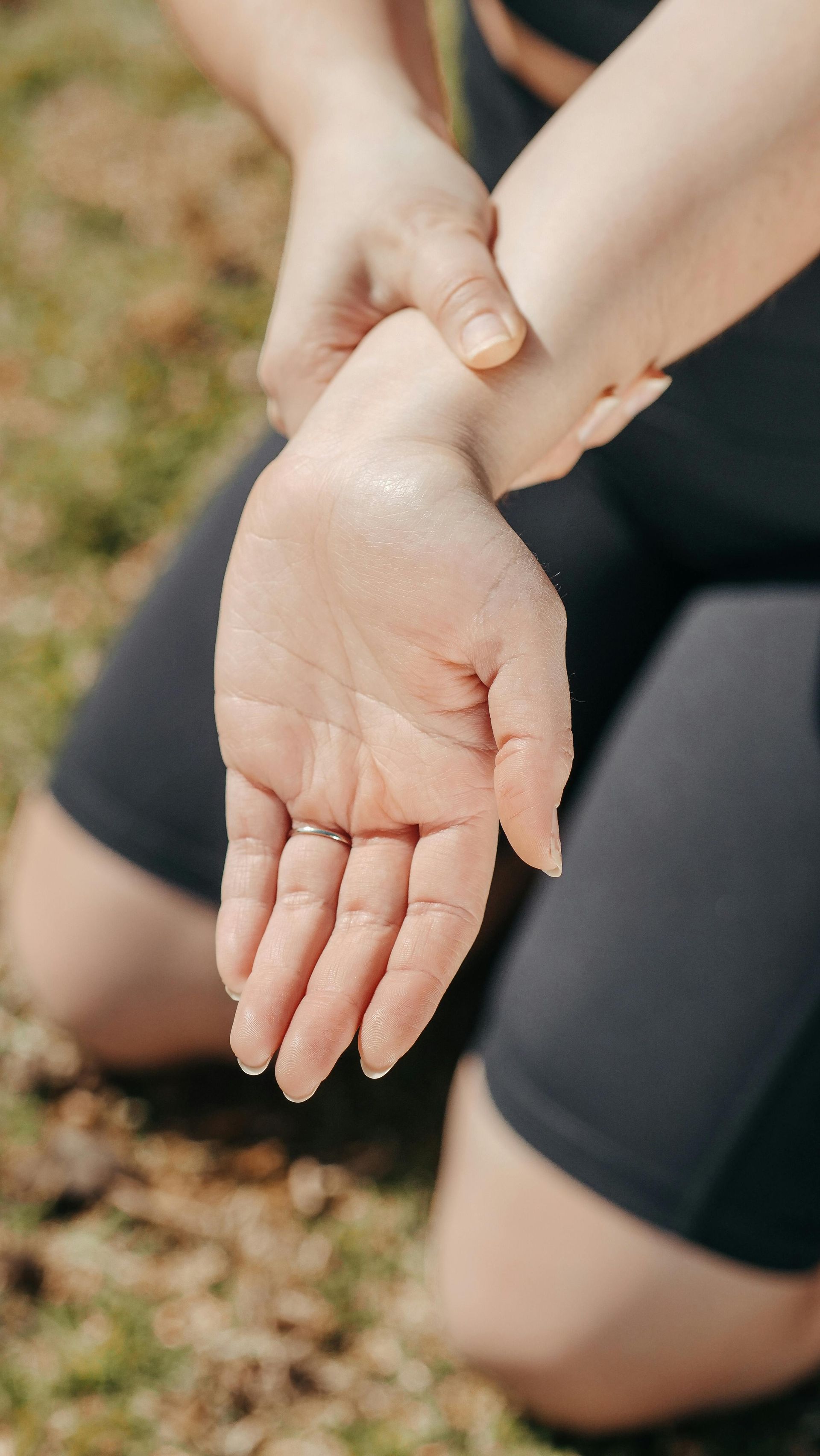 Person kneeling, holding their wrist, possibly injured. Outdoors, wearing black athletic wear.