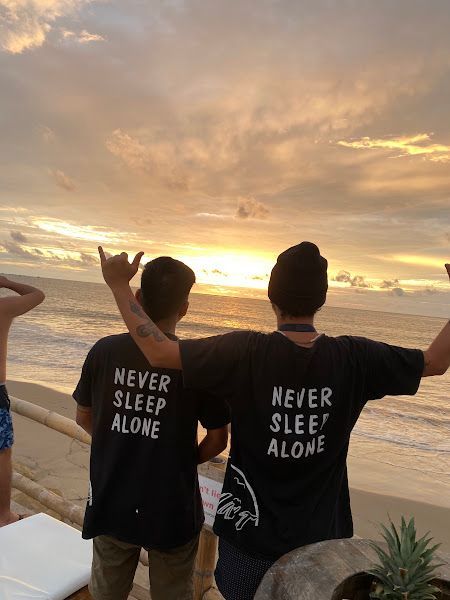 Two men wearing never sleep alone shirts stand on a beach