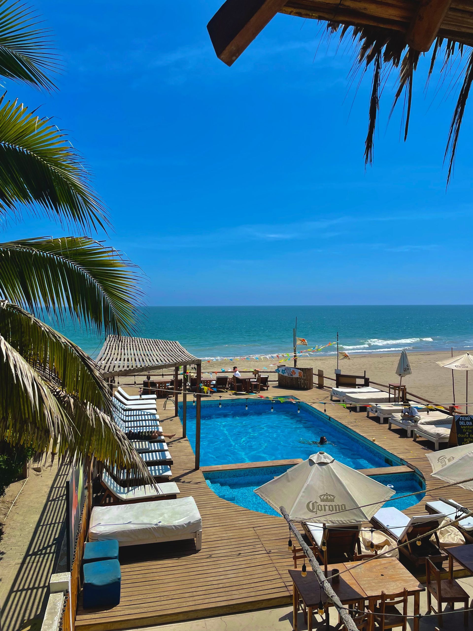 A large swimming pool is surrounded by chairs and umbrellas on a beach.