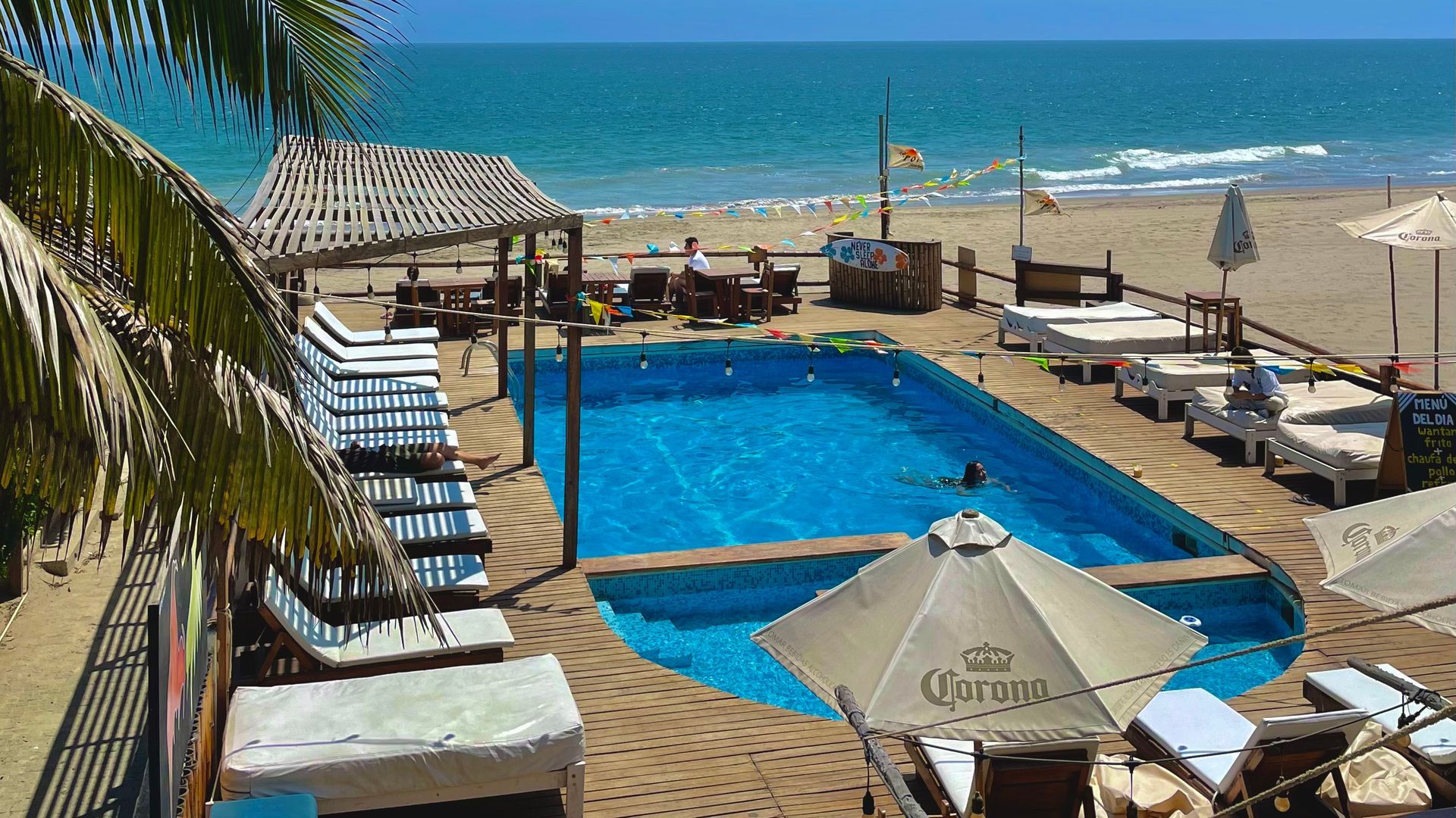 A large swimming pool surrounded by chairs and umbrellas on a beach.