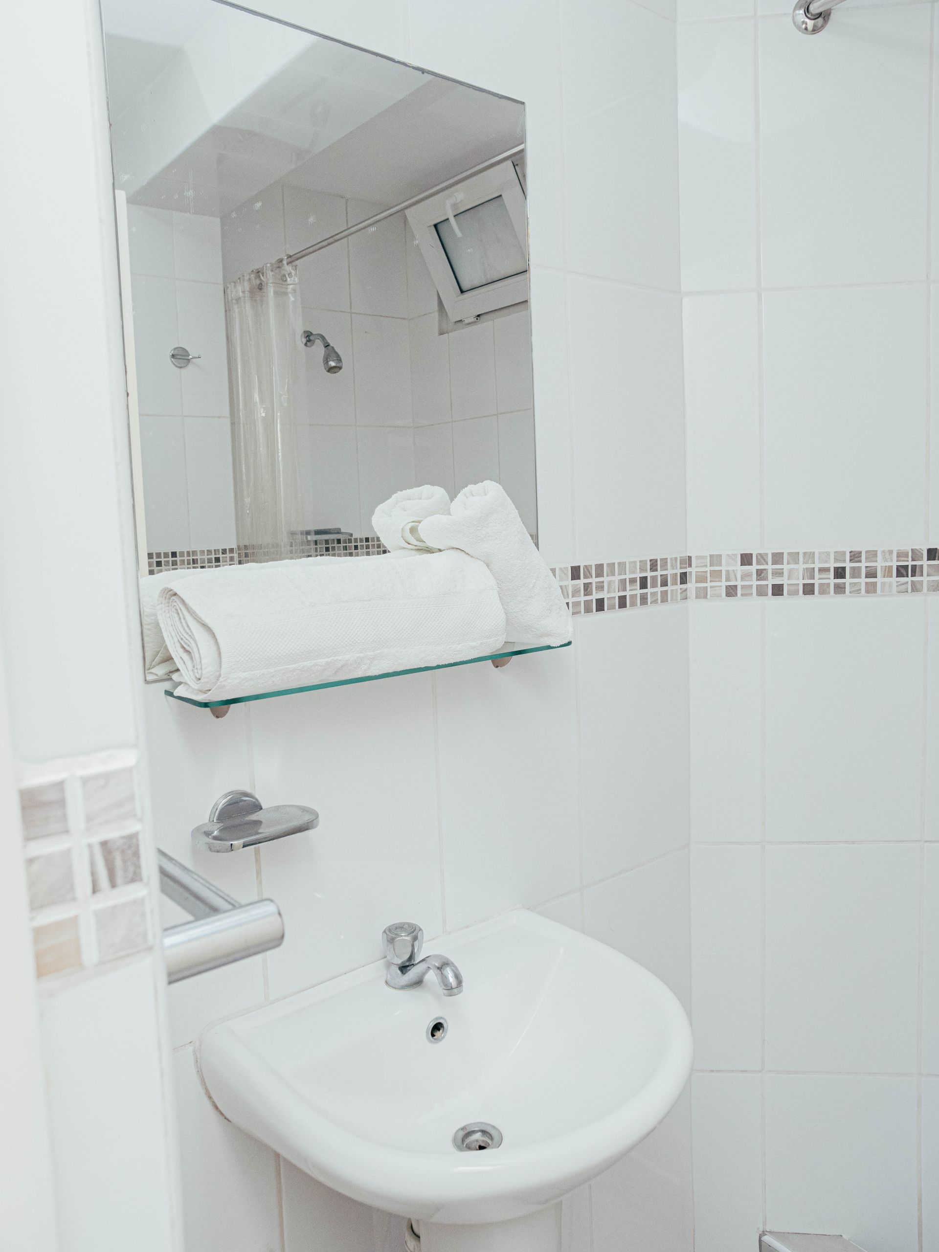 A bathroom with a sink , mirror and towels on a shelf