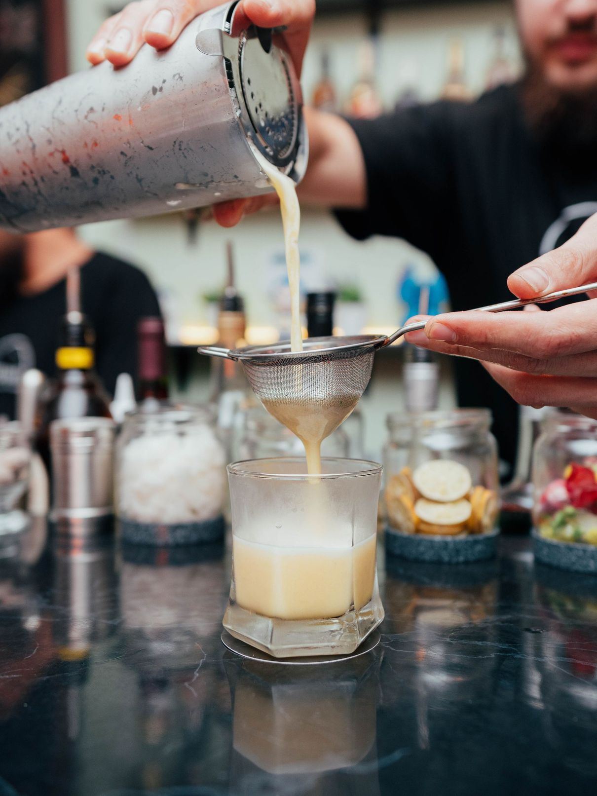 A bartender is pouring a drink through a strainer into a glass.