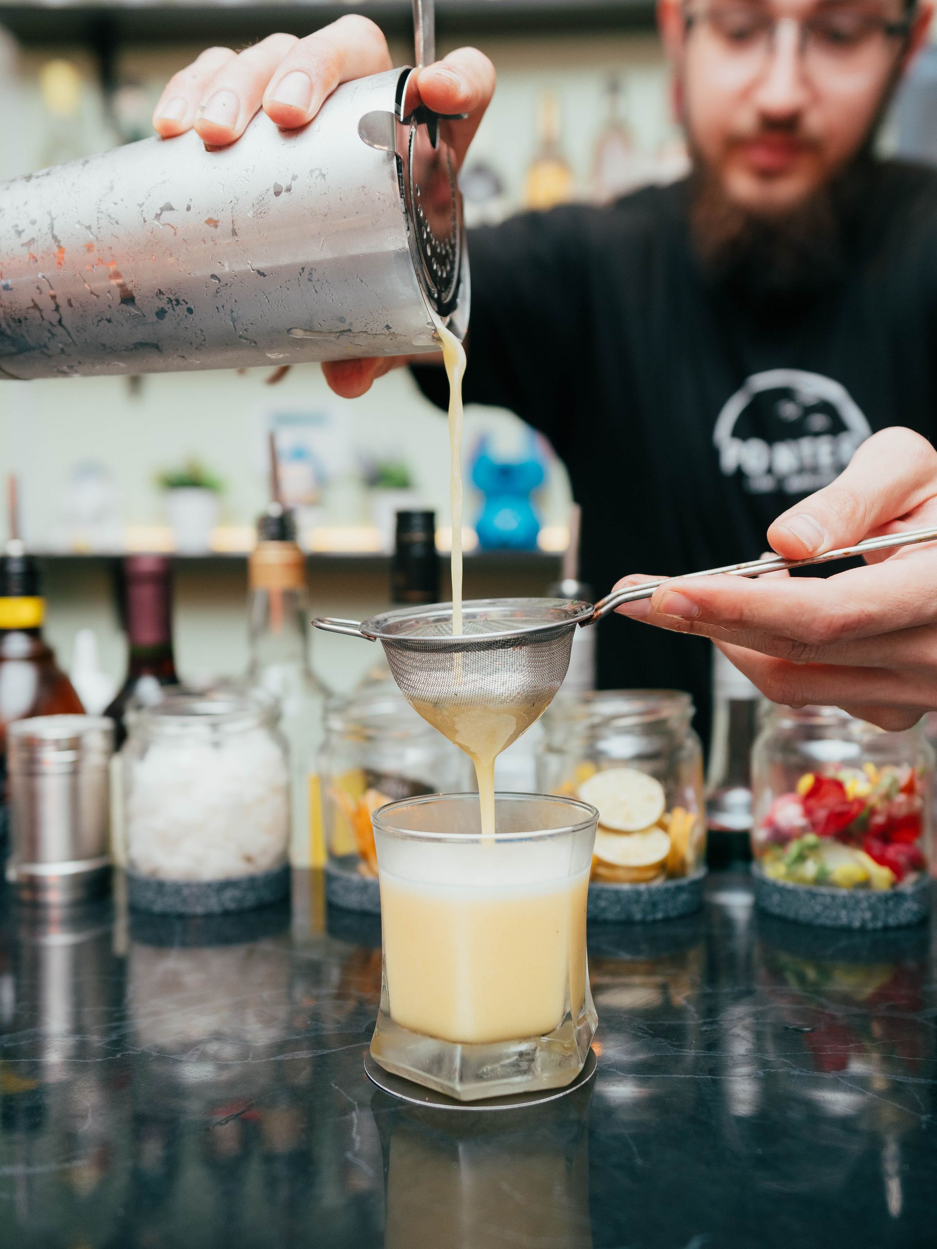 A man is pouring a drink through a sieve into a glass.