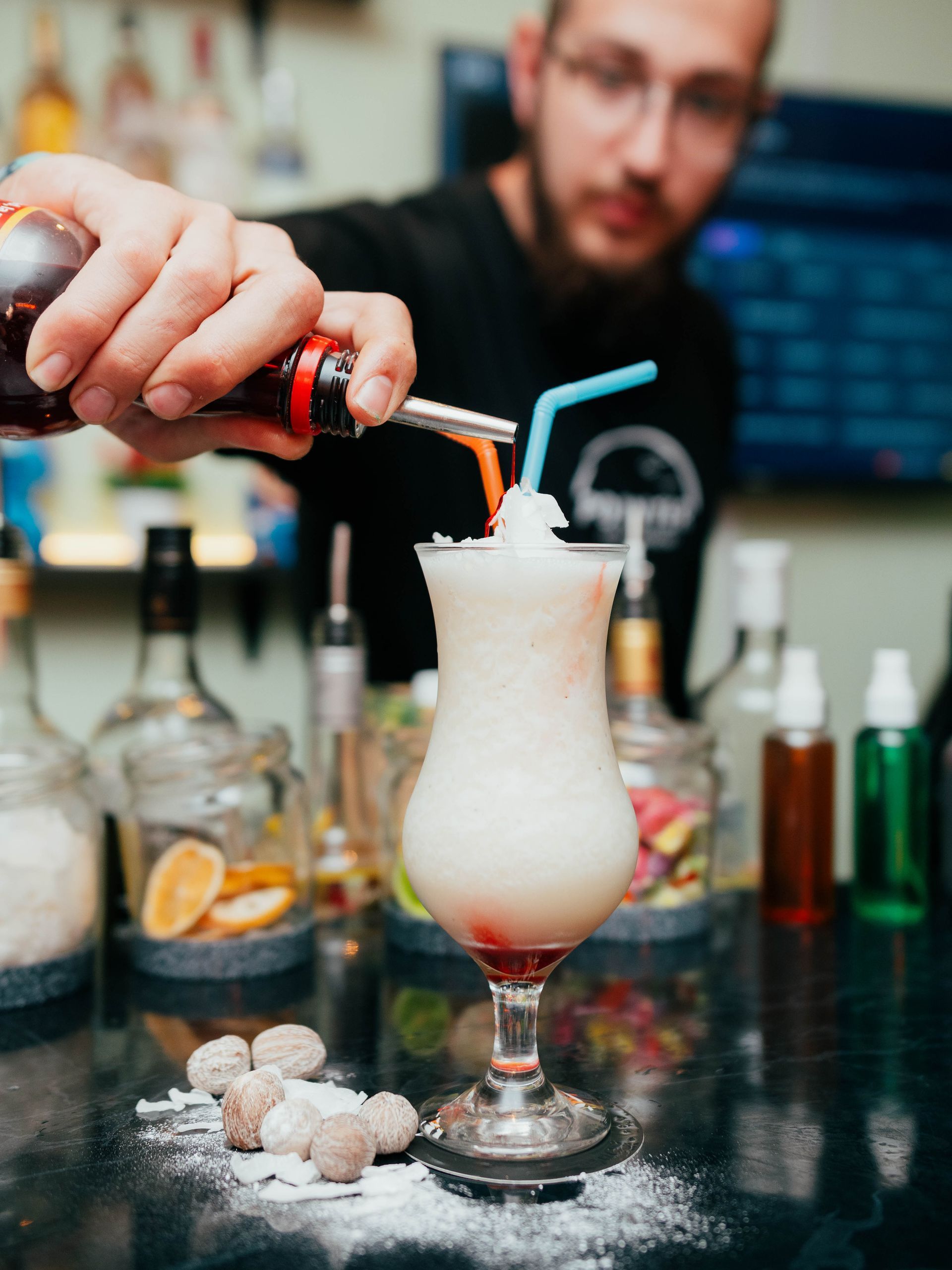 A man is pouring a drink into a glass with a straw.