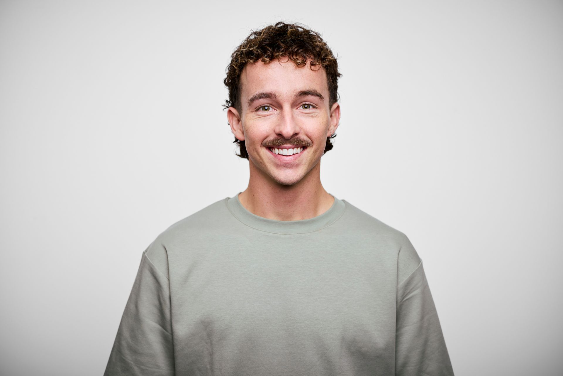 Smiling man with curly hair and mustache in a light green sweater.