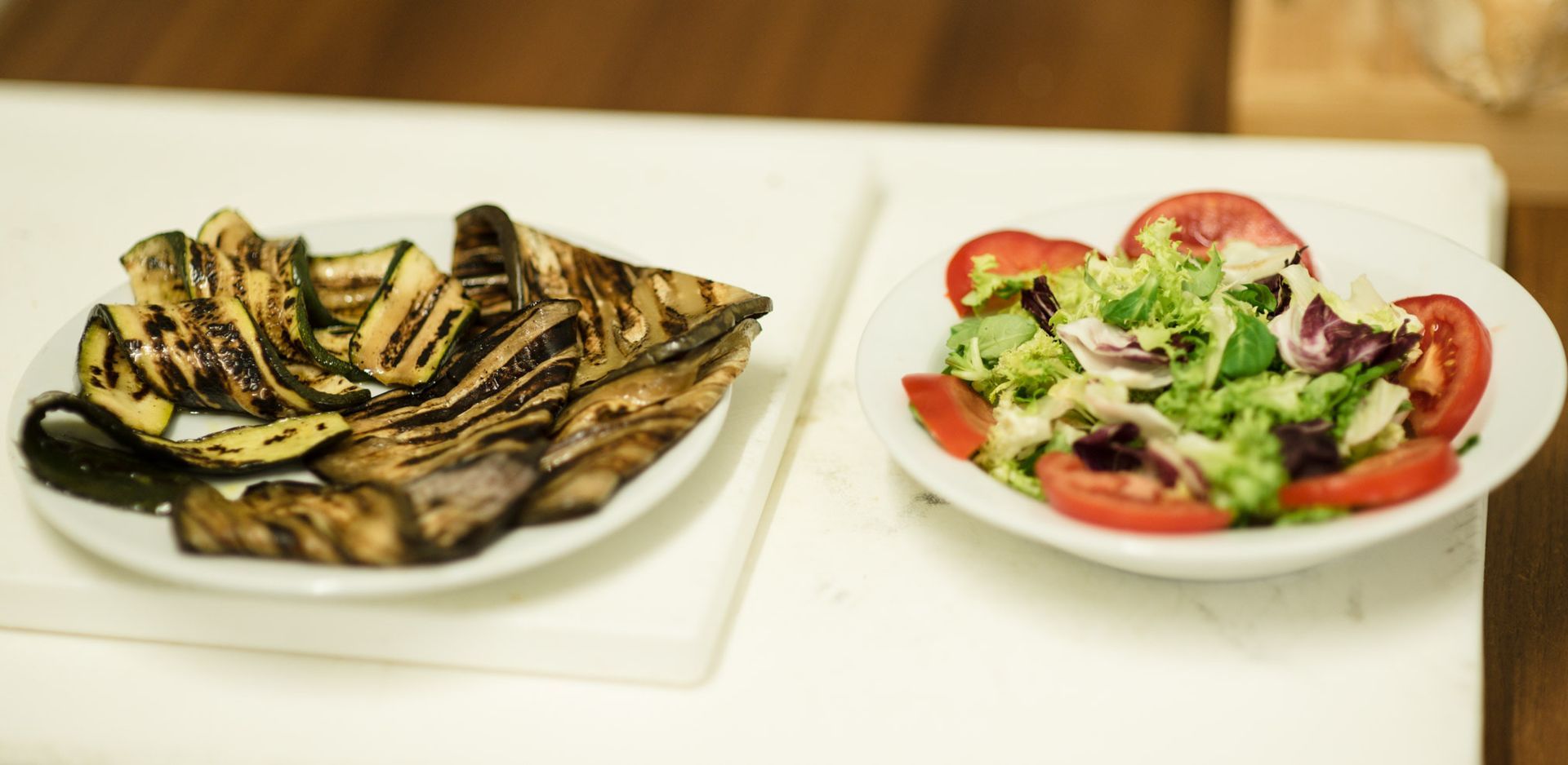 Verdure grigliate e insalata su piatti bianchi.