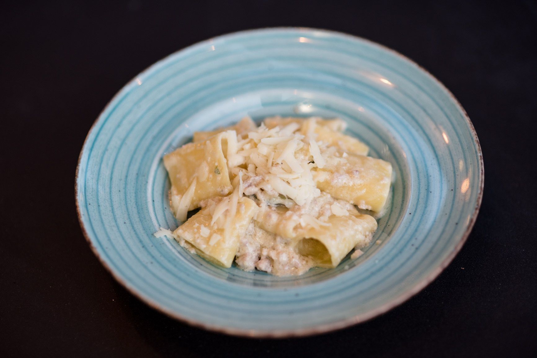 Piatto di pasta in una ciotola azzurra, con formaggio grattugiato sopra.