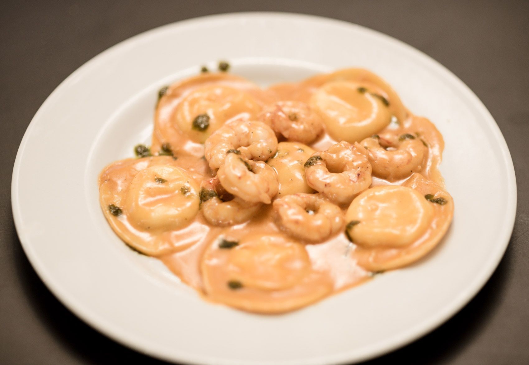 Piatto di pasta con gamberi e capperi in una cremosa salsa all'arancia su un piatto bianco.