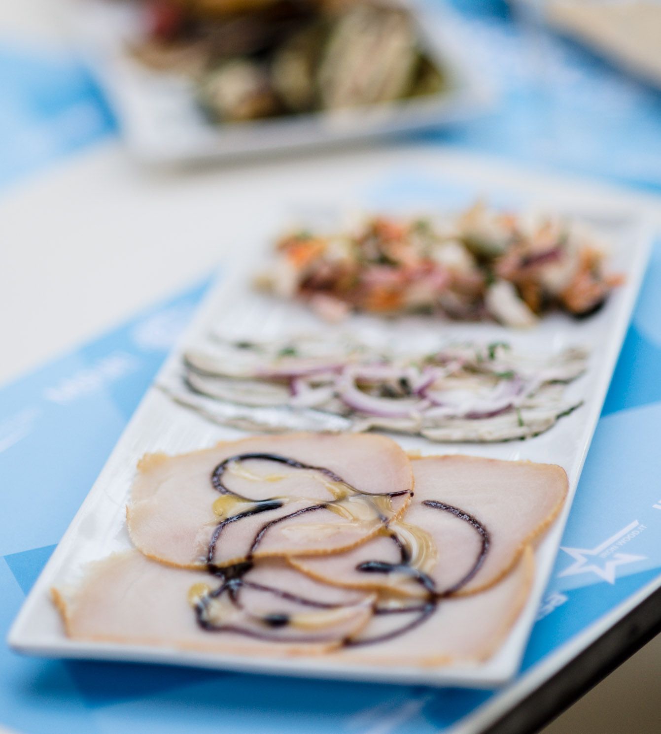 Piatti di antipasti a base di carne, pesce e frutti di mare, conditi con salse, disposti su un tavolo blu.