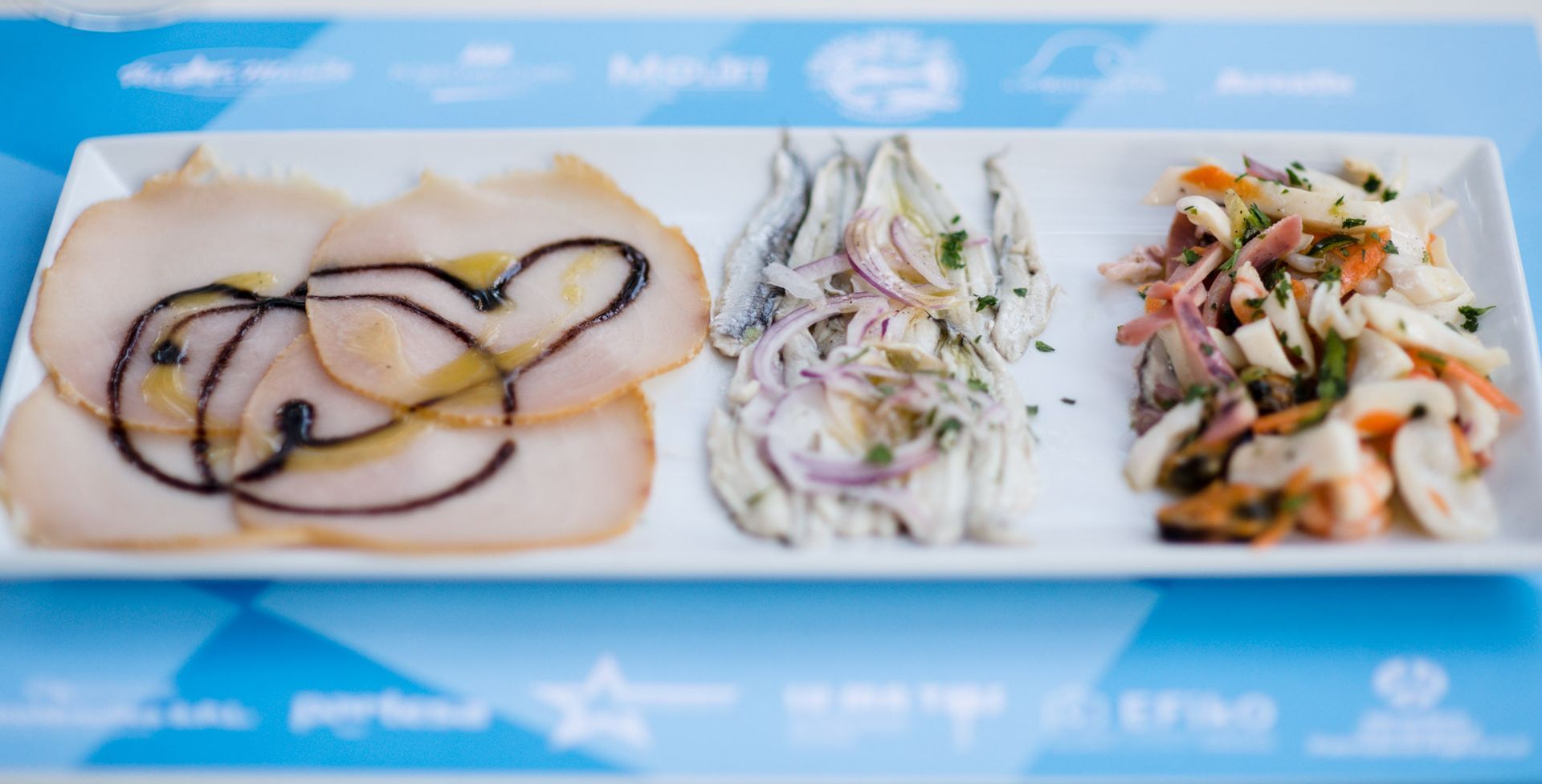 Piatto di antipasti di mare: pesce affettato con glassa balsamica, acciughe con cipolle e insalata di mare.