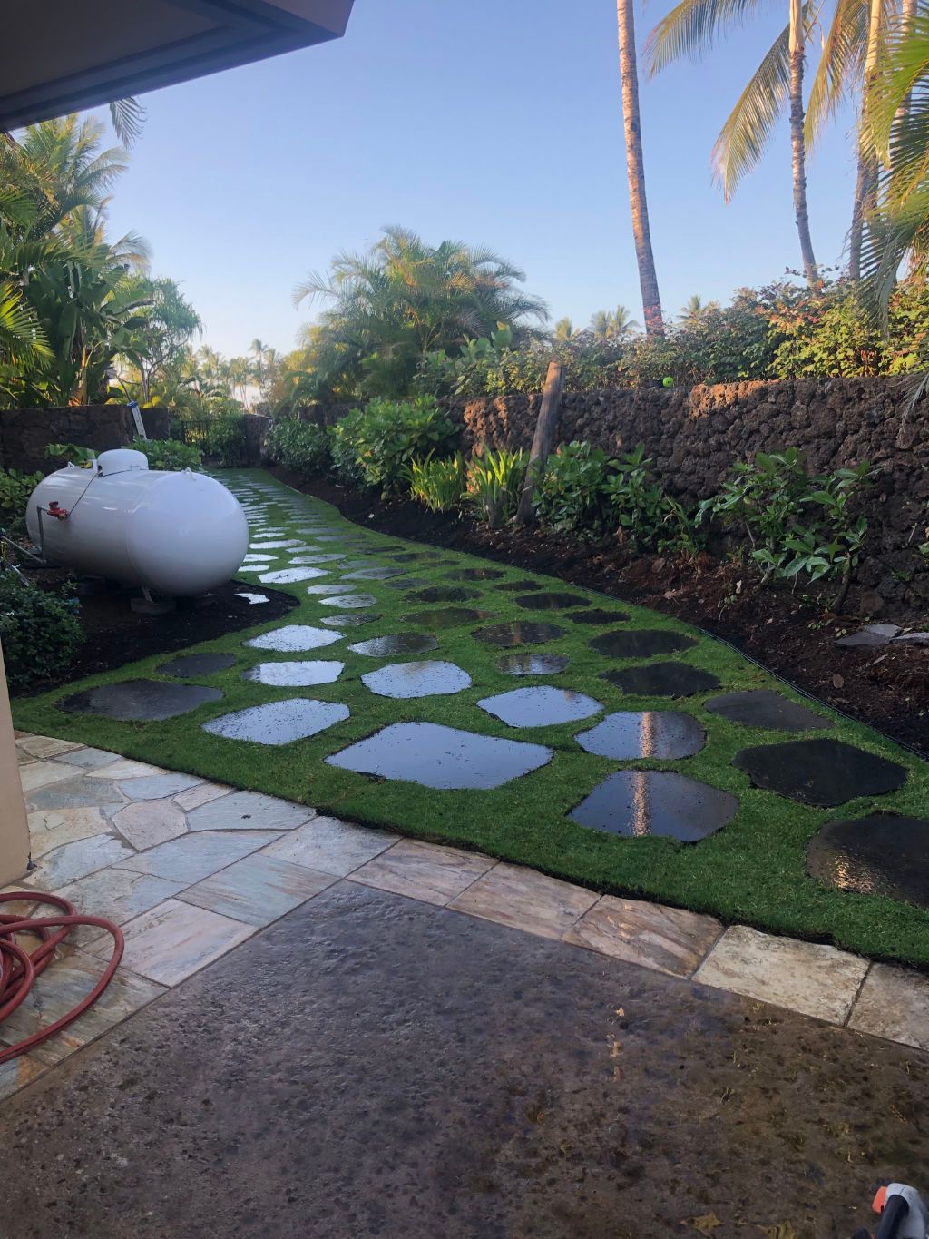 Landscape installation project showing lawn with stepping stones and a propane tank in the background.