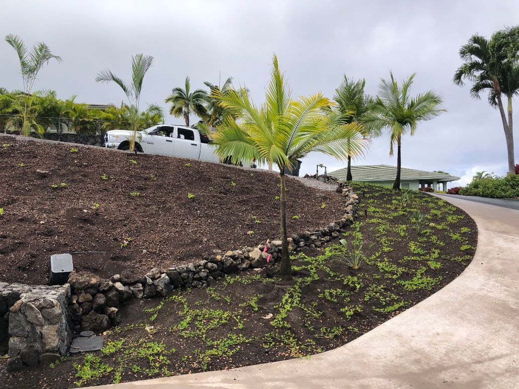 A white truck is parked on the side of a hill showing a landscape contractor project. 