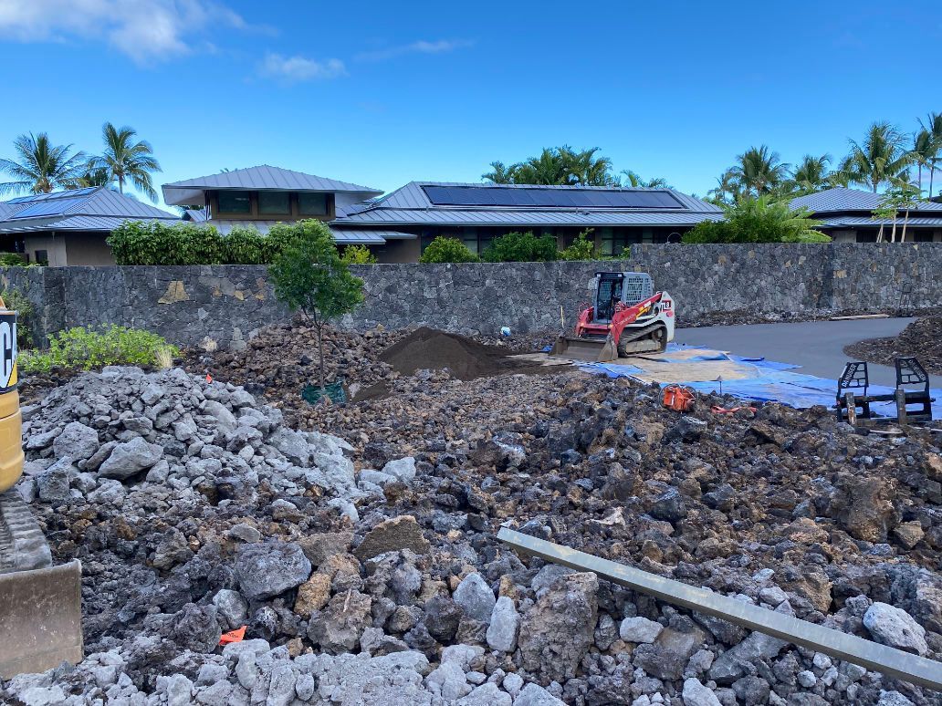 A construction site with a lot of rocks and a house in the background.