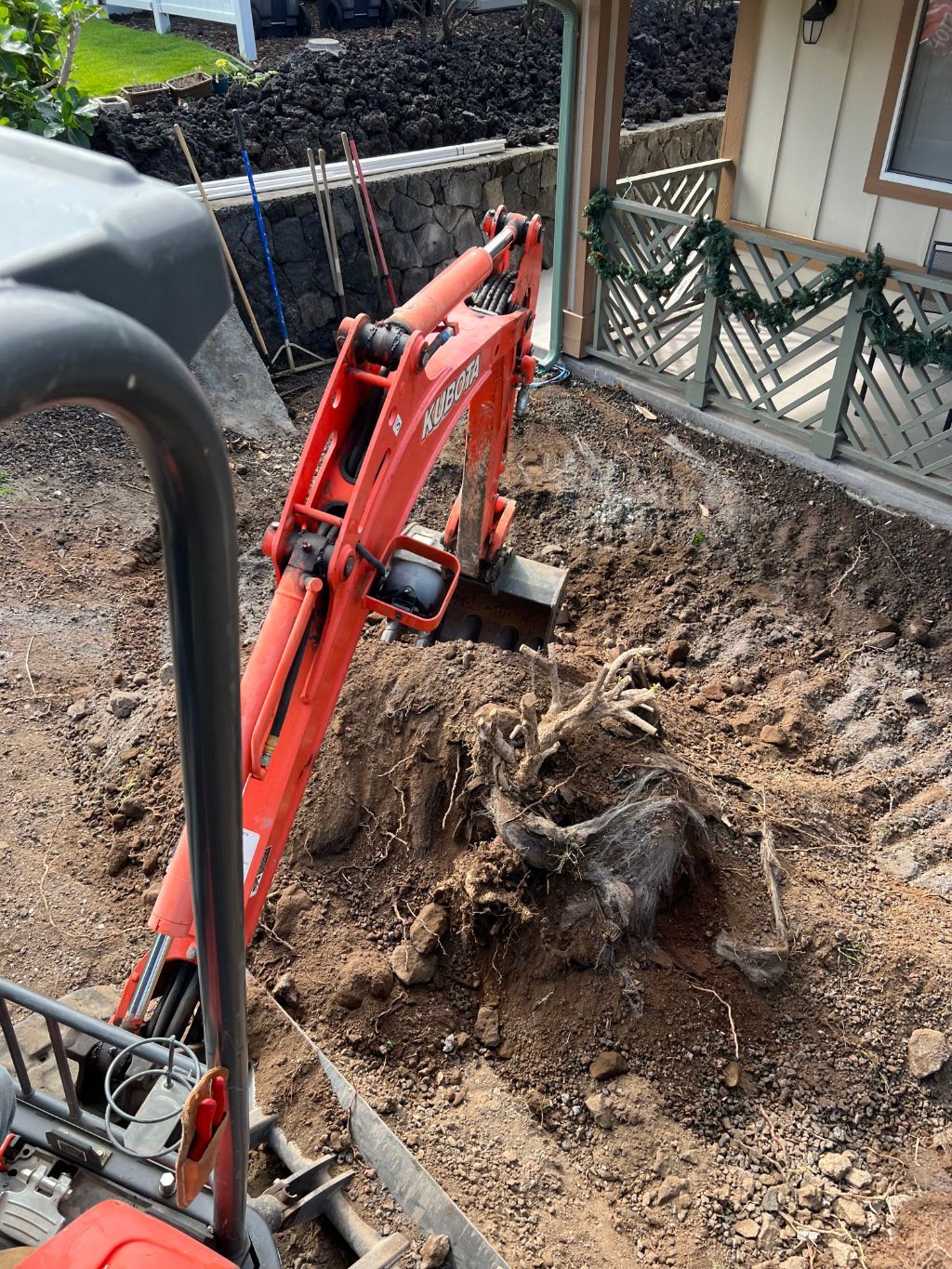 A red excavator is digging a hole in the dirt in front of a house for excavating. 