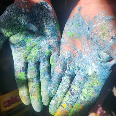 Hands covered in colorful powder paint, palms open and facing up.