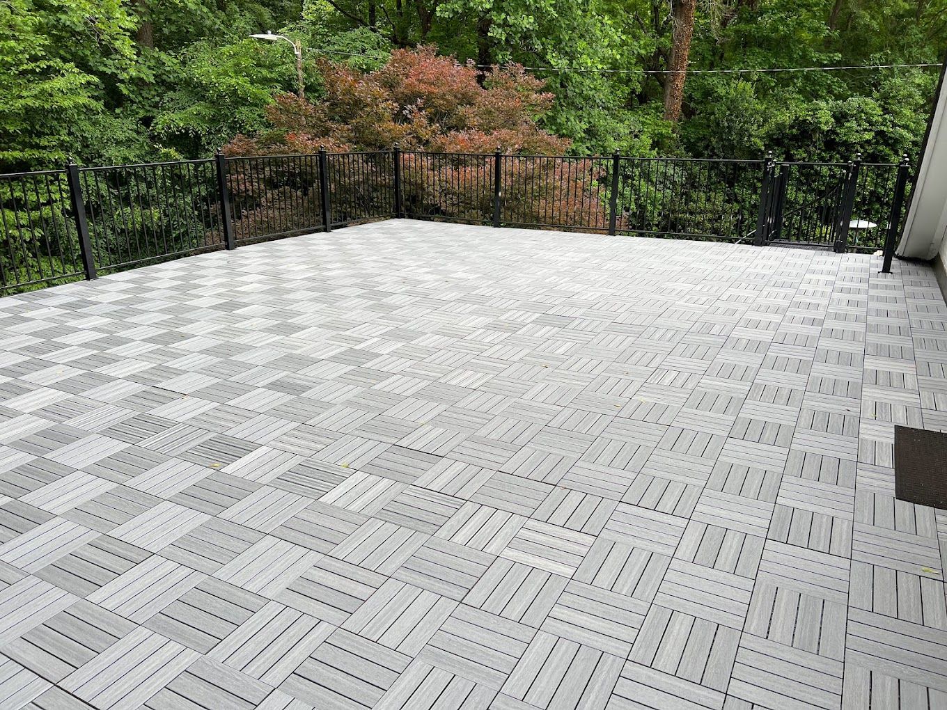 A large patio with a fence and trees in the background.