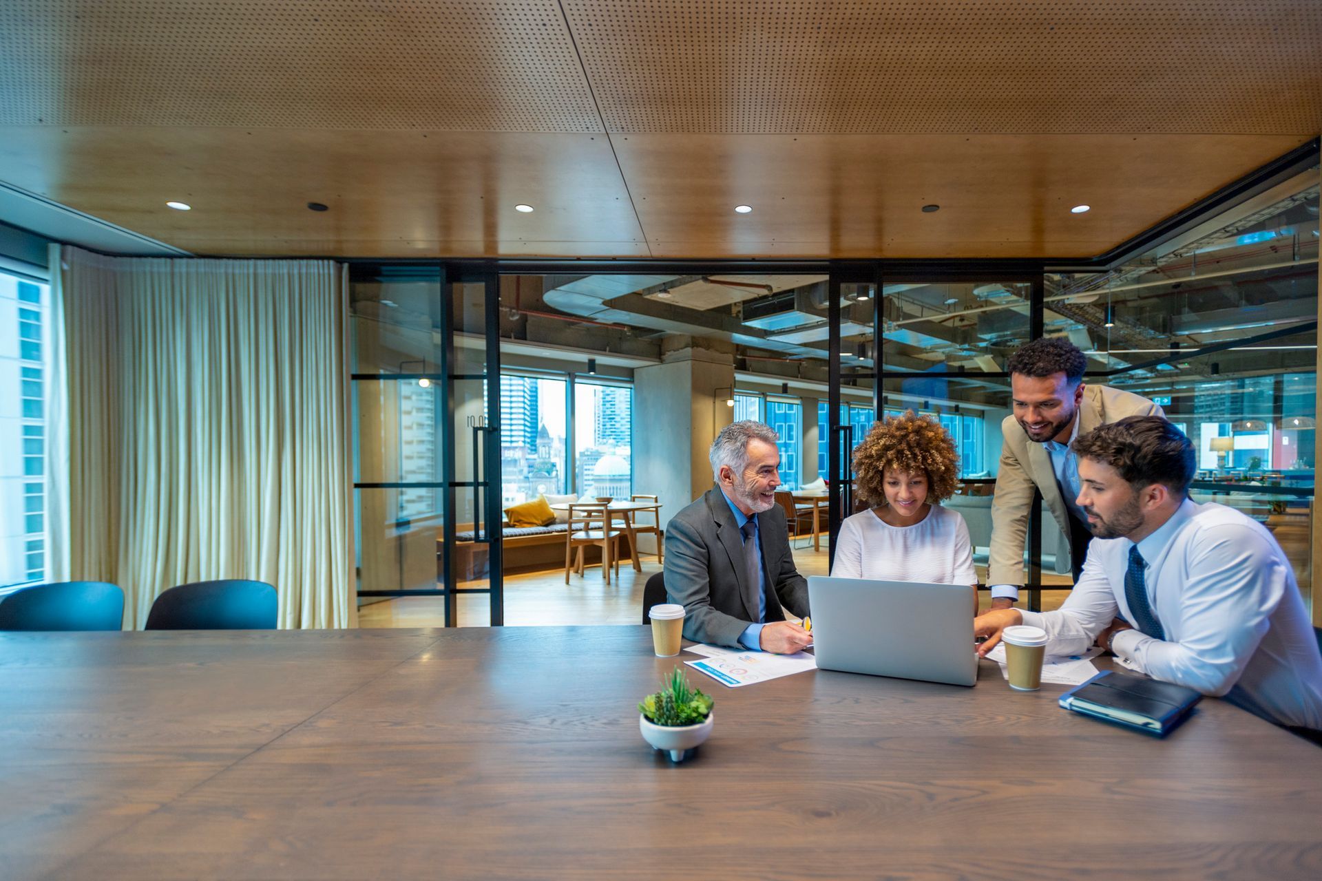 A group of business people are sitting around a table looking at a laptop computer.