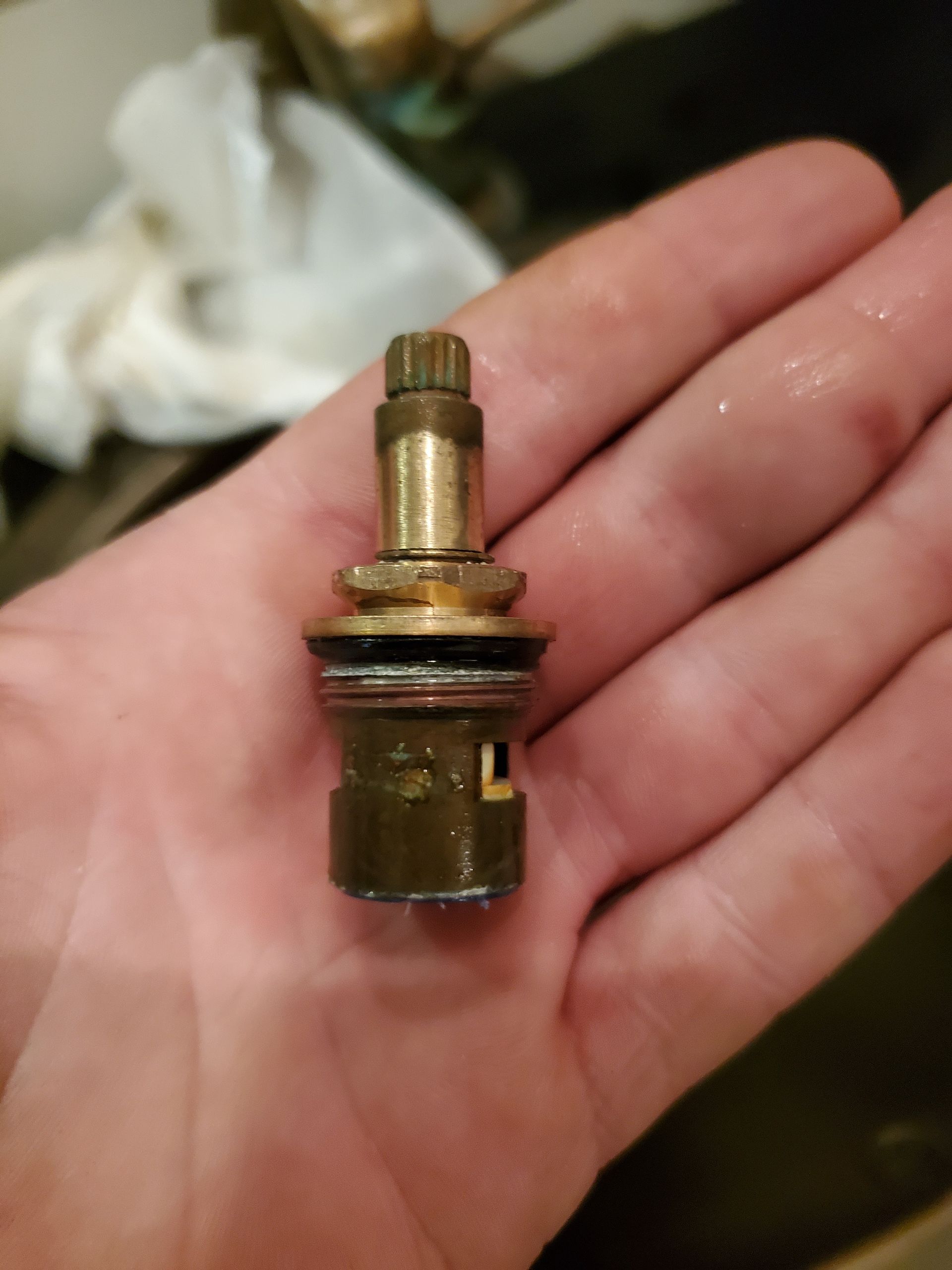 A disassembled faucet cartridge held in a person's palm, brass and worn looking.