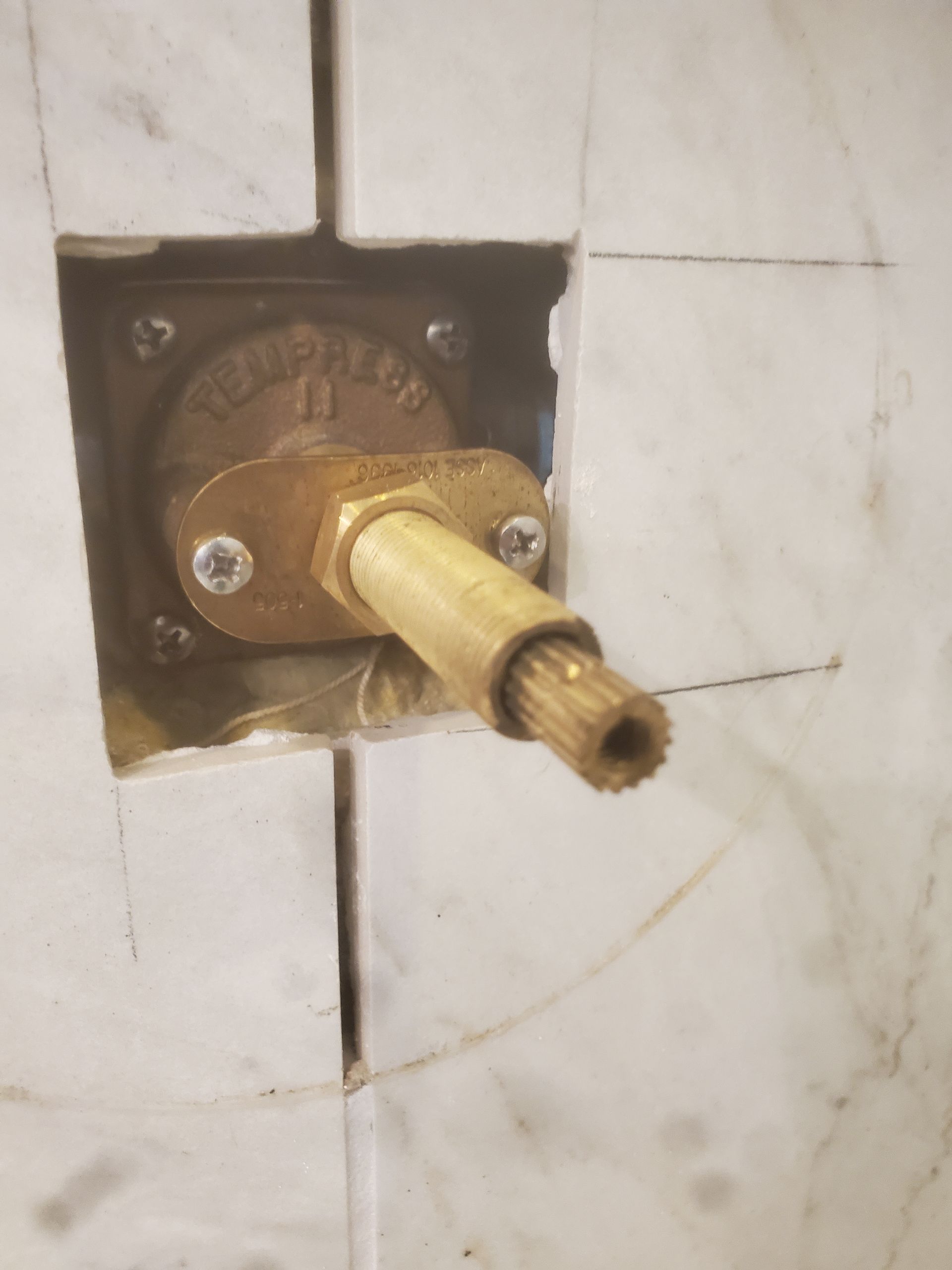 Close-up of a brass shower valve protruding from white marble tiles. Valve is labeled