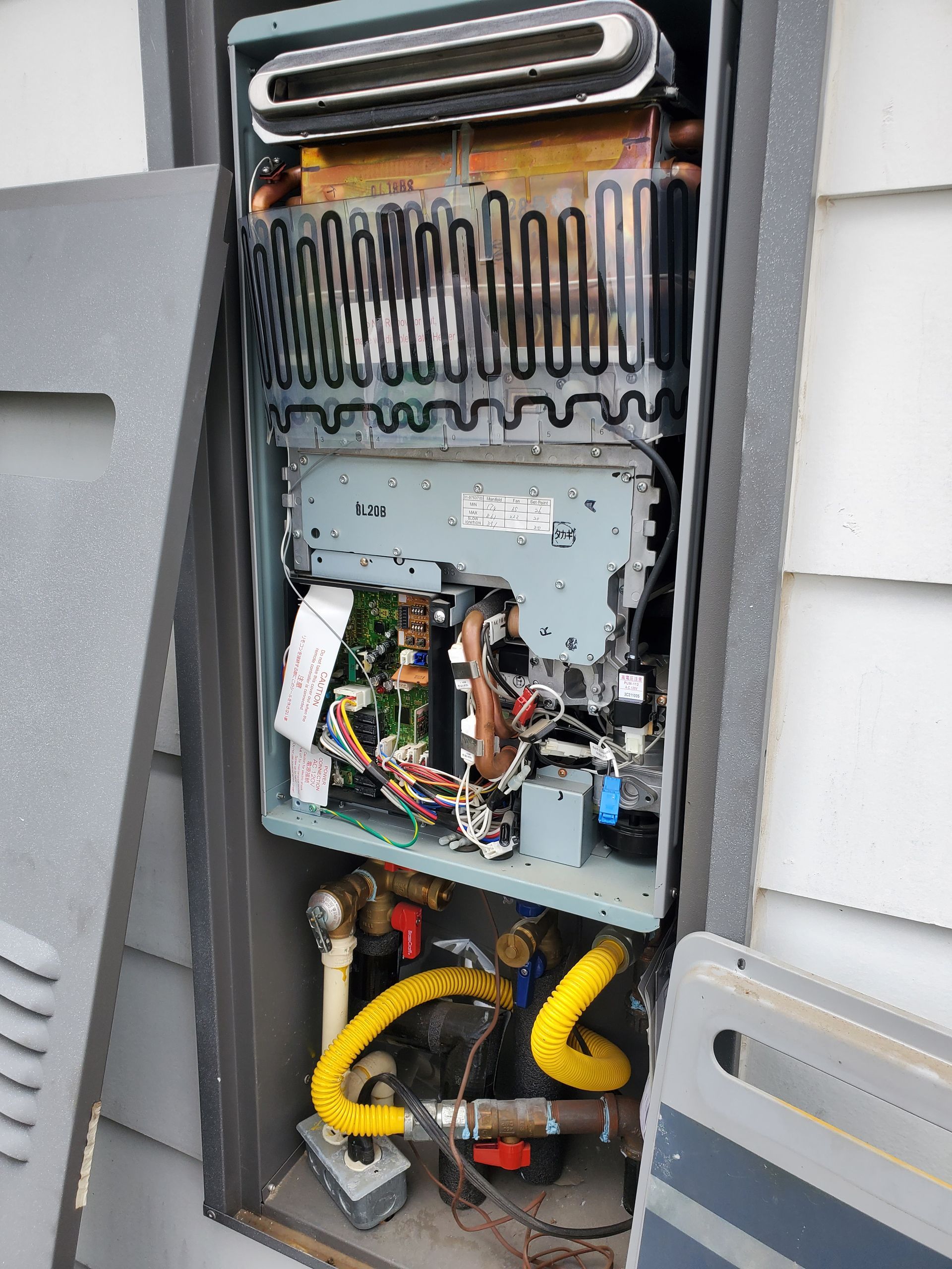 Open outdoor tankless water heater, showing internal components including copper coils, wiring, and gas lines.