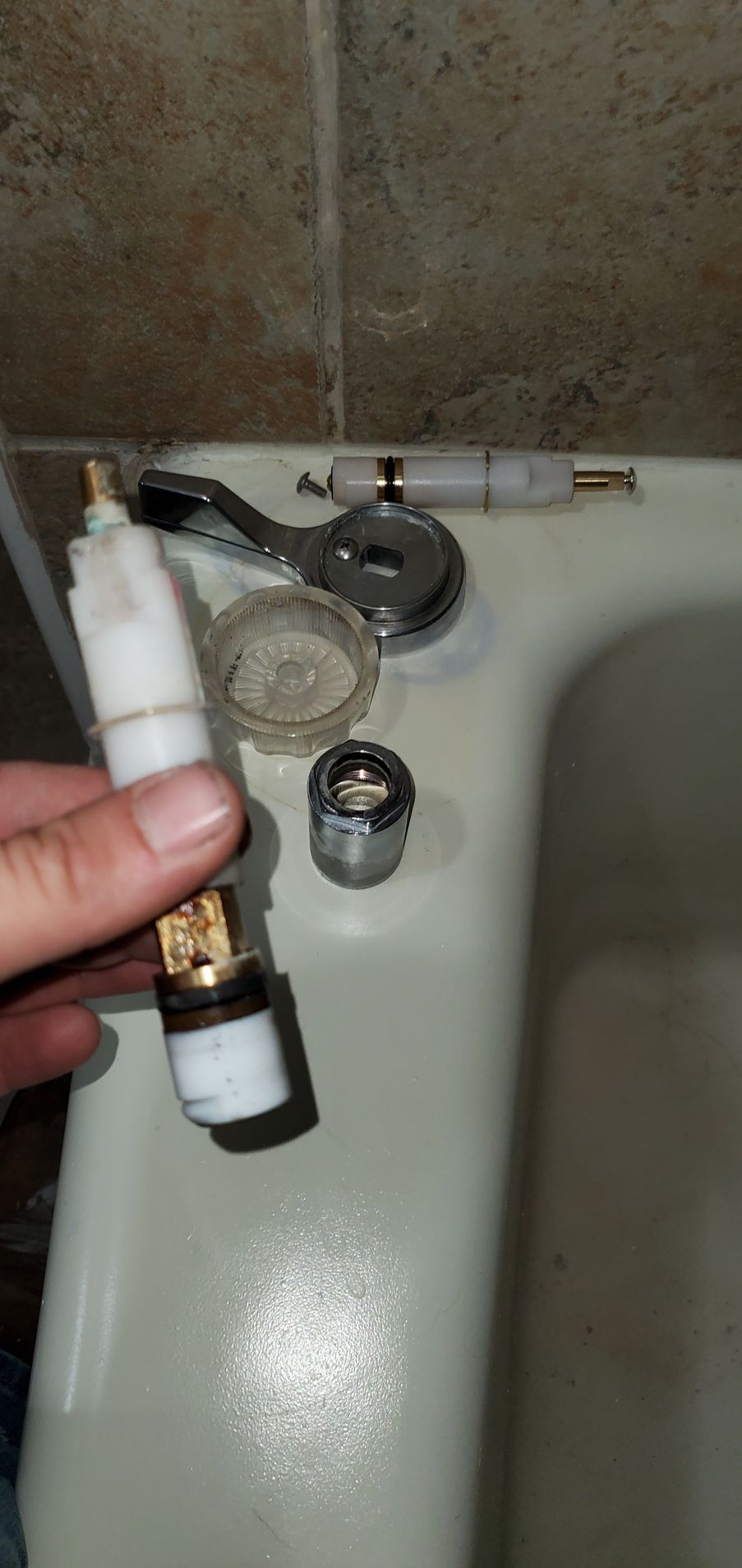 Person holds faucet valve stem; other faucet parts rest on bathtub rim.