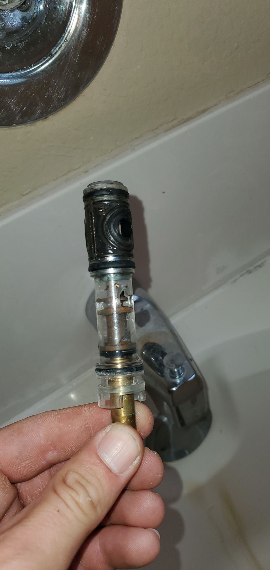 A person holding a removed faucet valve above a bathtub. The valve has a brass end.