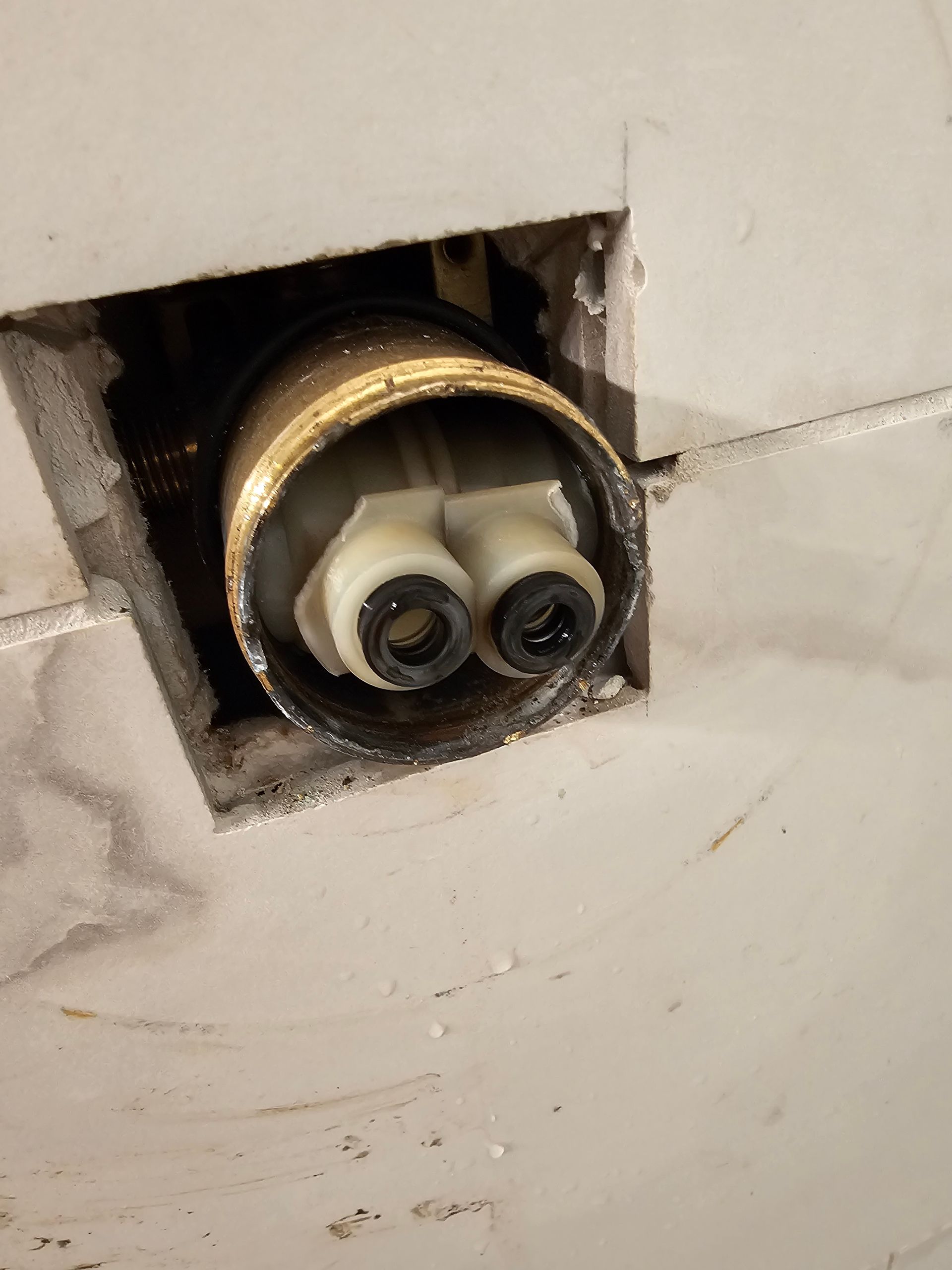 View of a brass faucet fixture from inside a wall cavity, showing two water outlets.