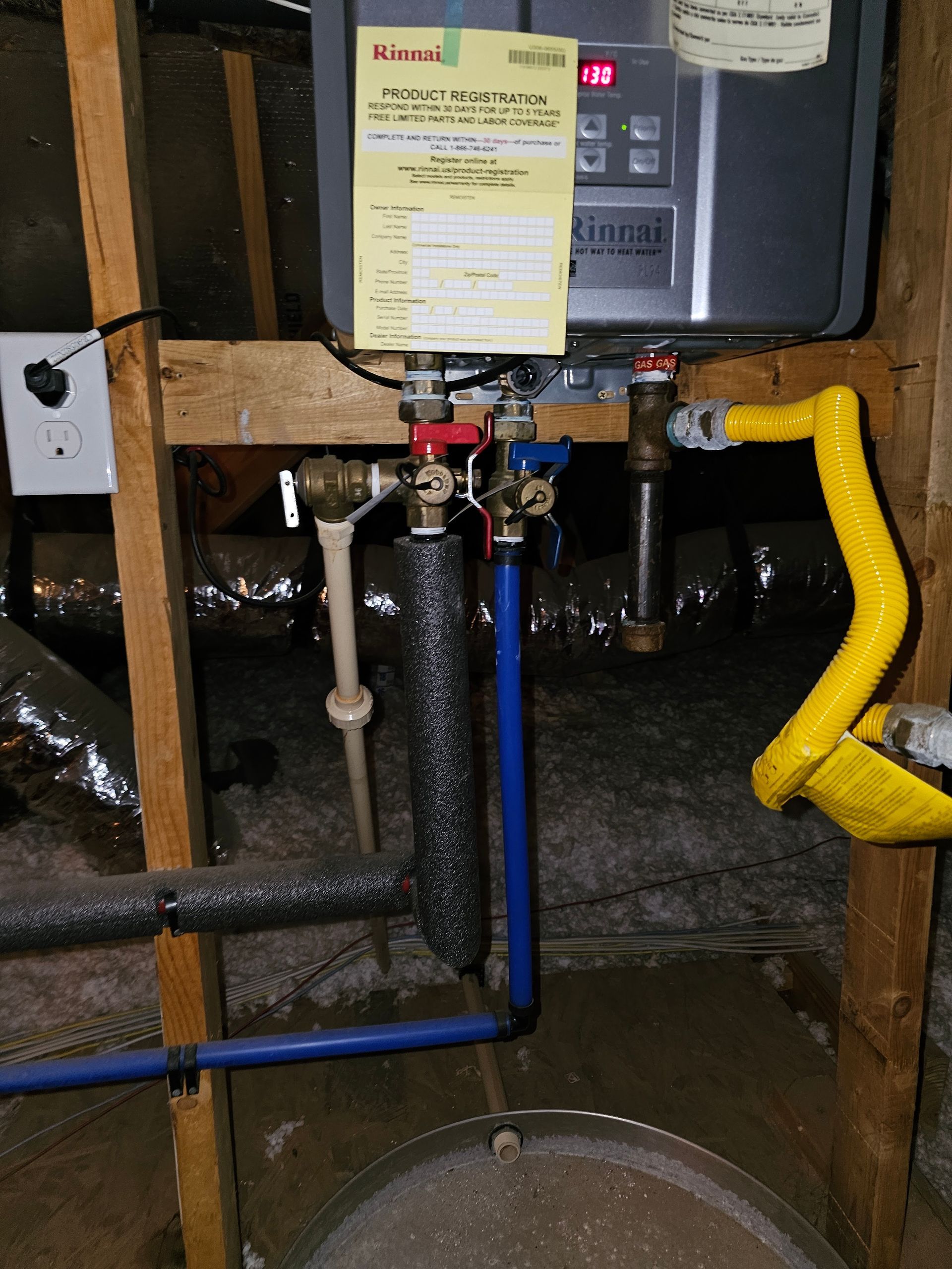 Rinnai water heater with pipes and valves installed on a wooden frame in a crawlspace.