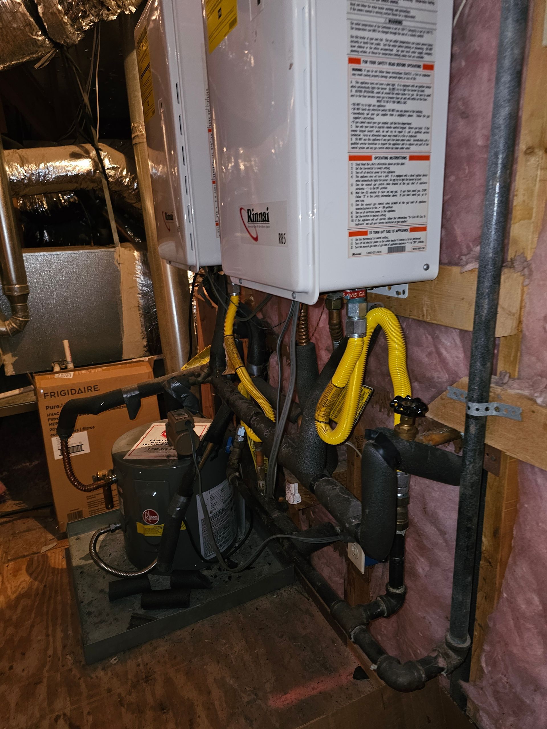 Two white water heaters mounted on a platform with associated black pipes and yellow gas lines in a mechanical room.