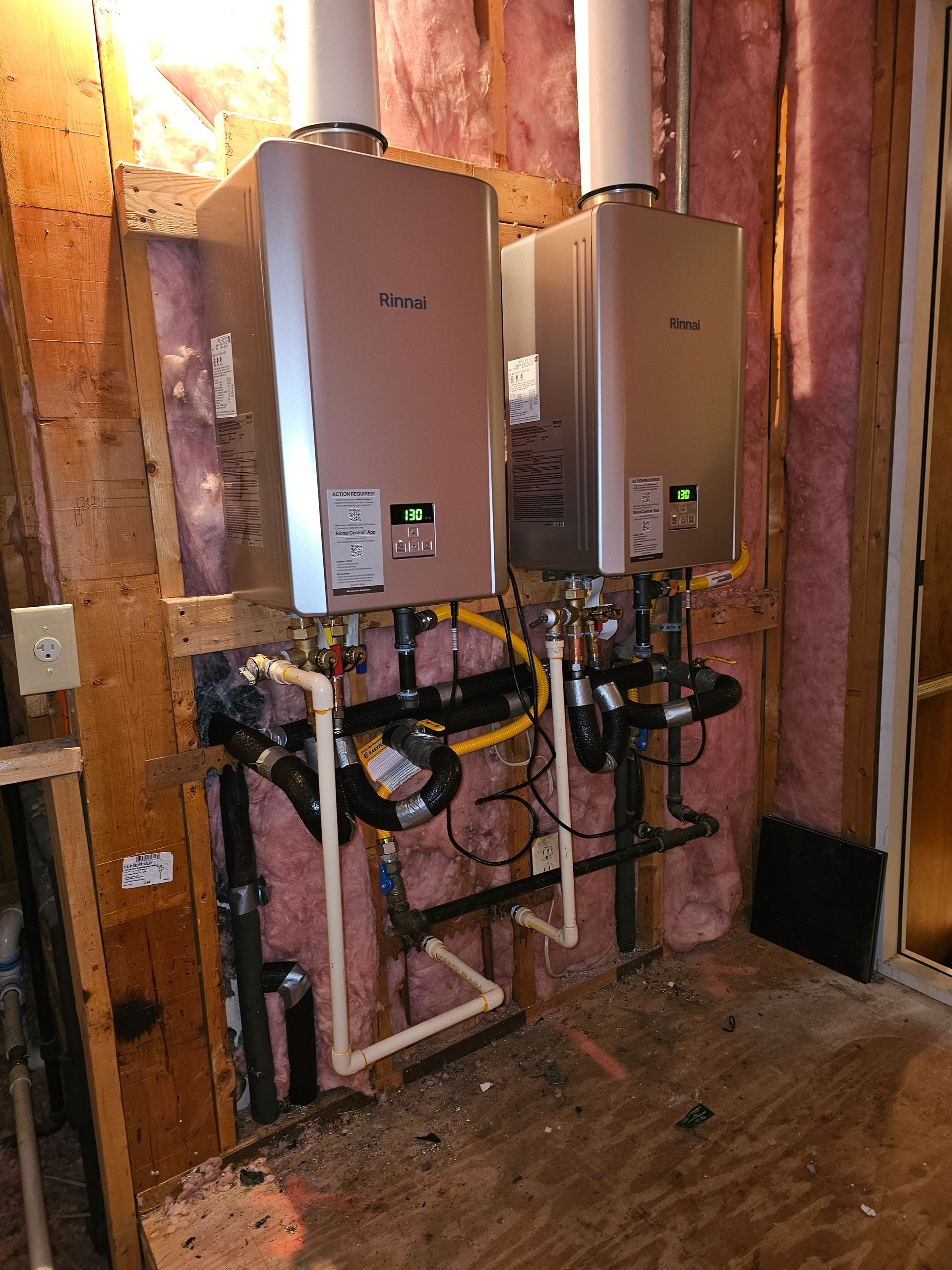 Two wall-mounted water heaters with white vent pipes, black pipes, and beige walls.