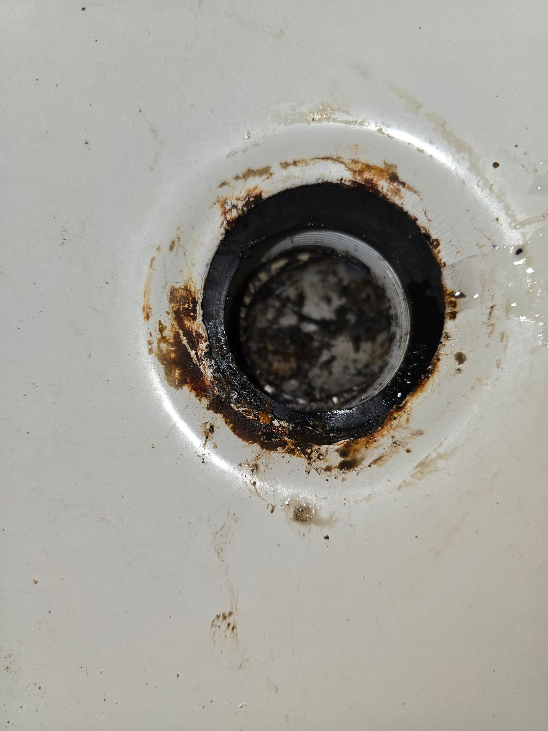 Close-up of a white bathtub drain with brown residue around the opening.