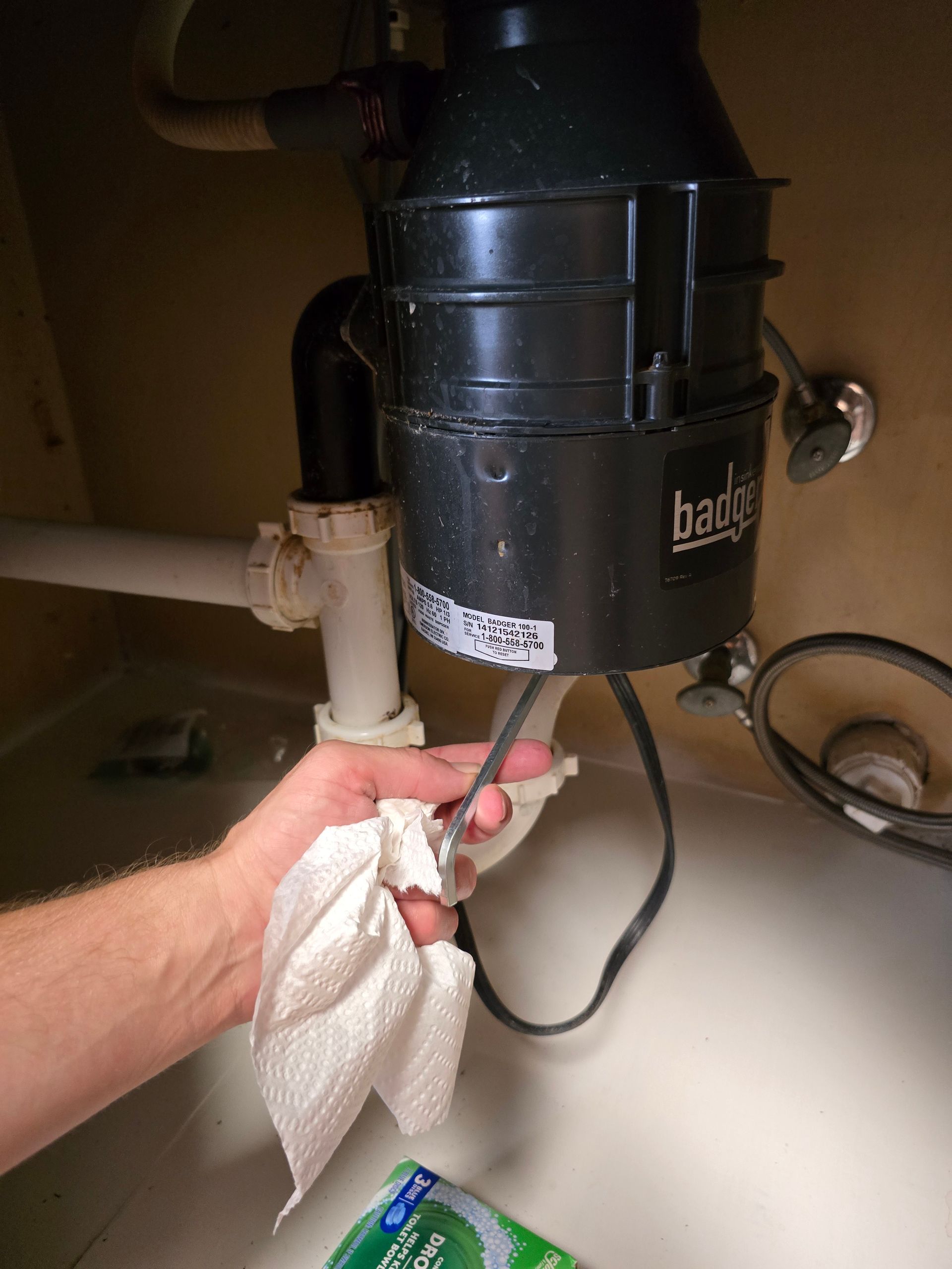 Hand holding a paper towel near a black garbage disposal under a sink.