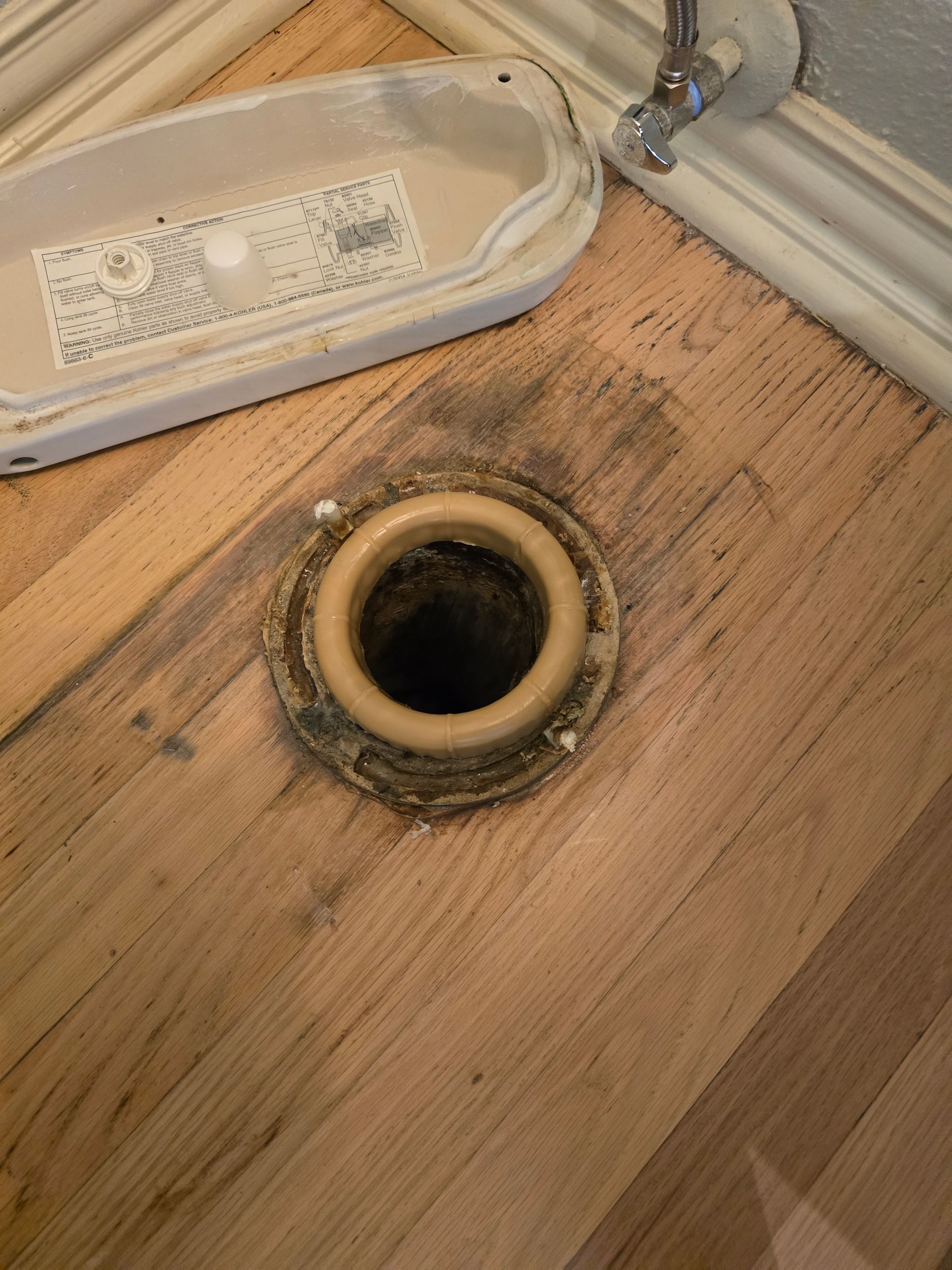 Toilet base removed, revealing drain pipe and damaged wood flooring.