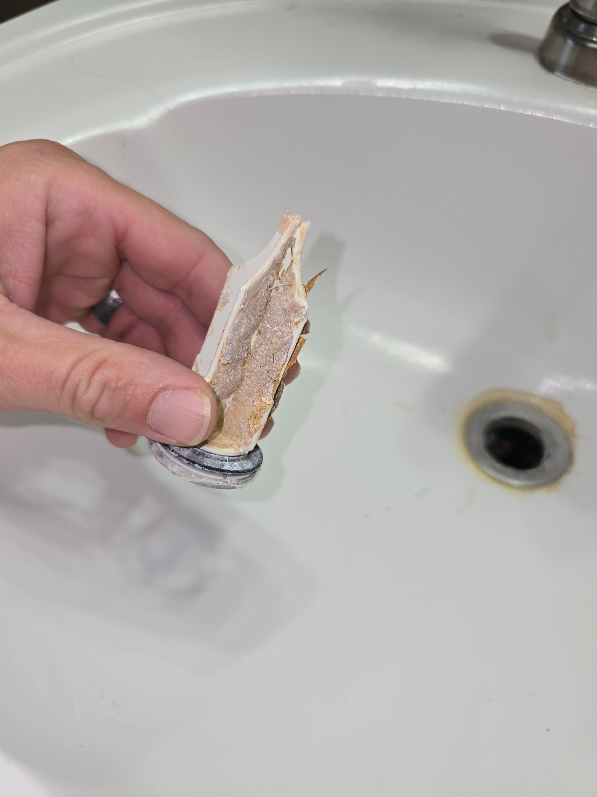 Hand holding a broken ceramic sink stopper over a white sink.