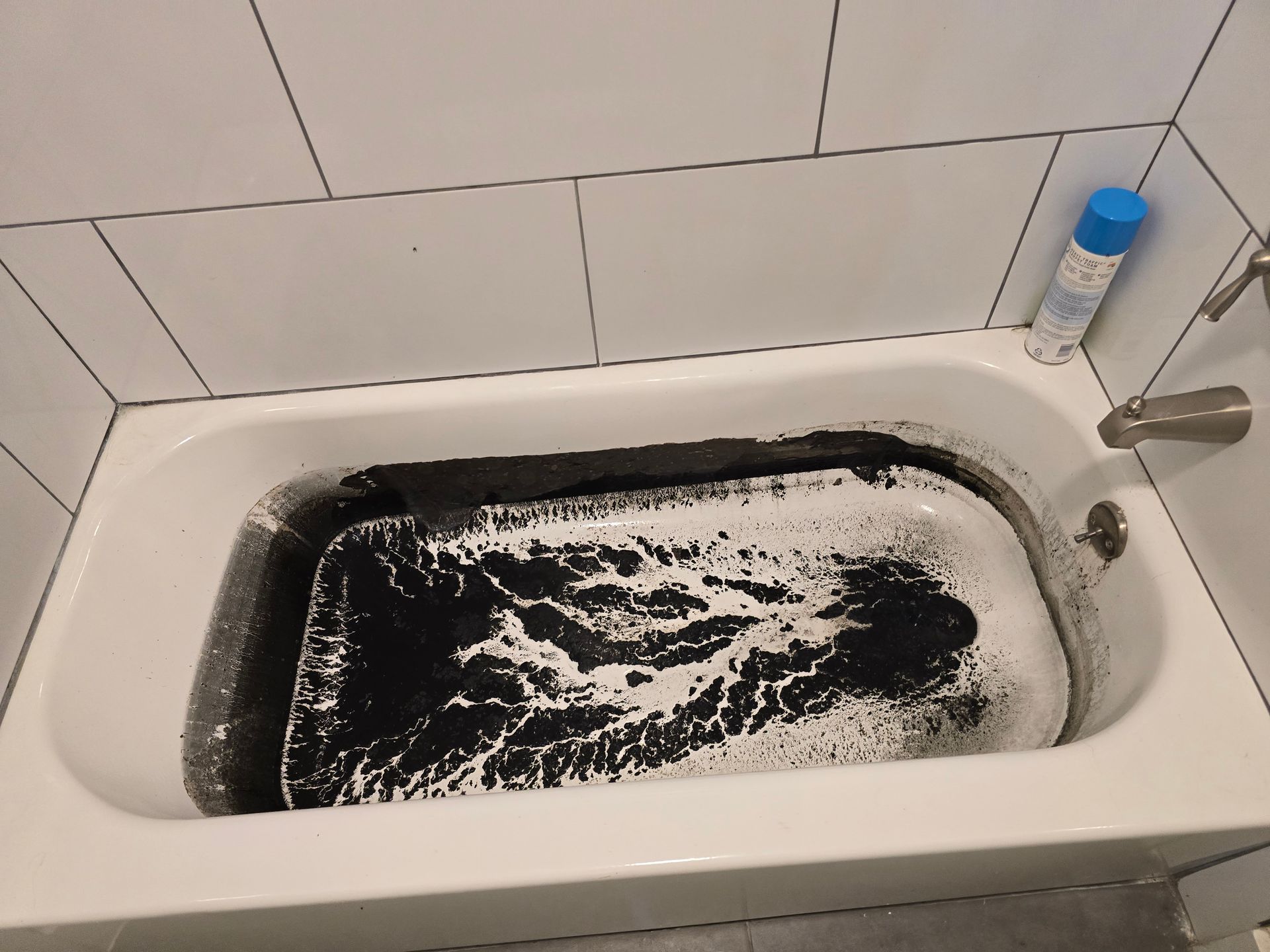 Black and white rug soaking in a bathtub with white tiled walls and a spray bottle.